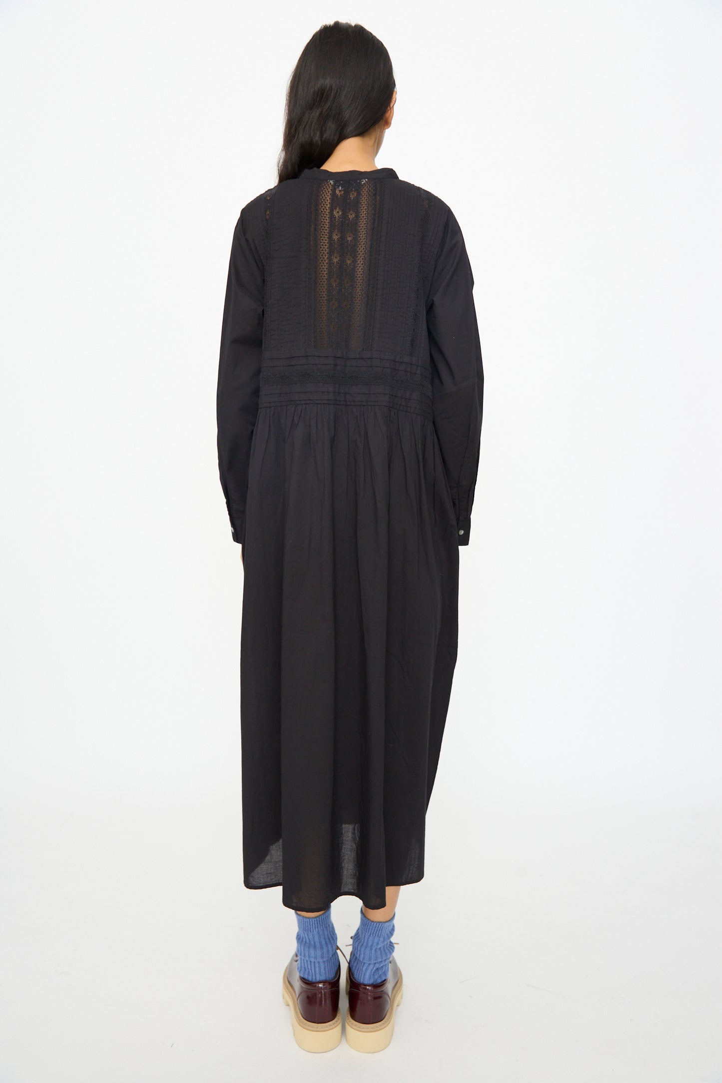 A person stands facing away, wearing the Ichi Antiquités India Cotton Dress in Black, styled with blue socks and platform shoes, against a plain white background.