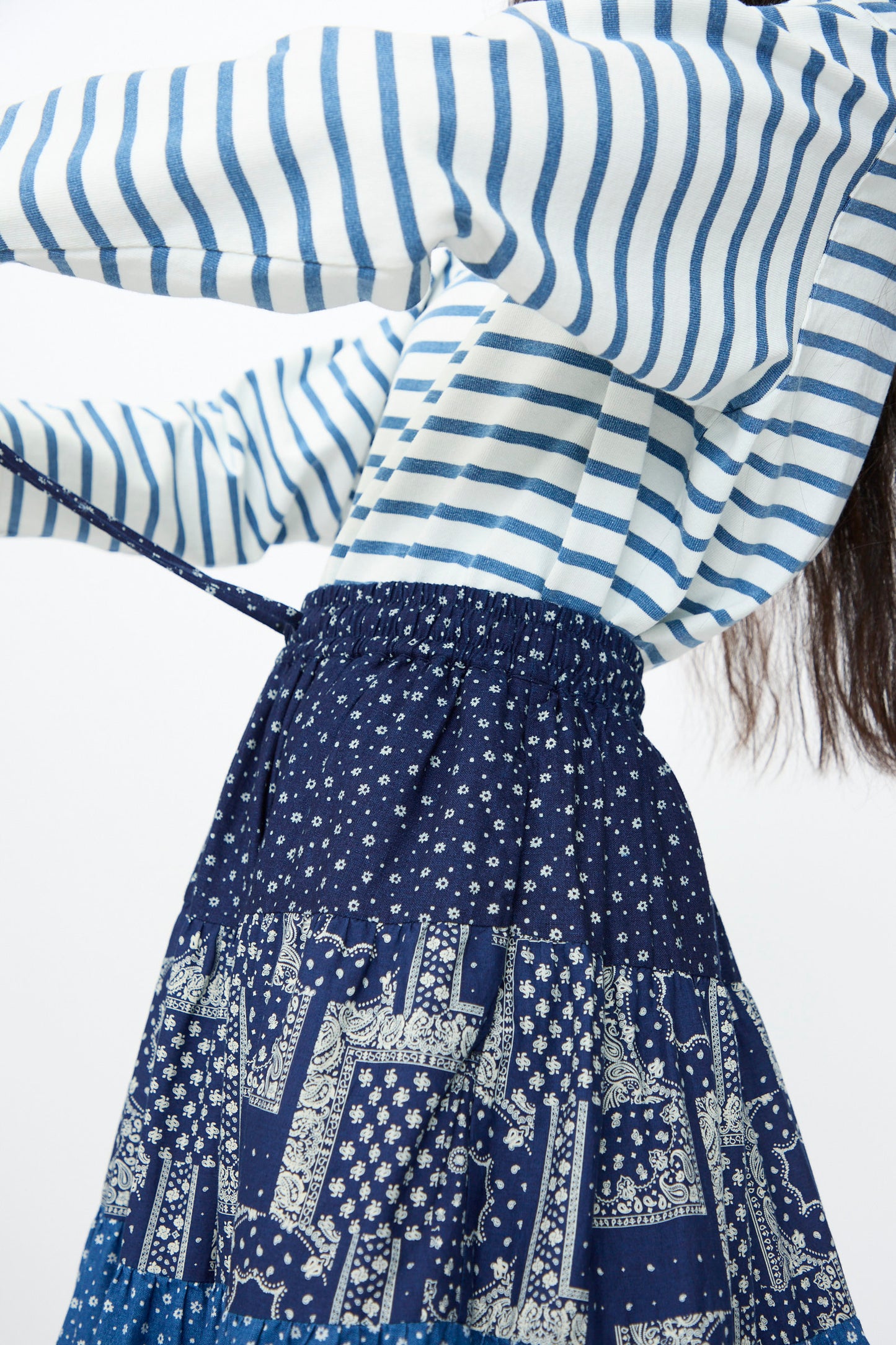 Person wearing a blue and white striped long-sleeve shirt and the Indigo Flower Skirt in Navy Mix by Ichi Antiquités, featuring an elasticated waistband. Upper body and part of the skirt are partially visible while adjusting the tie.