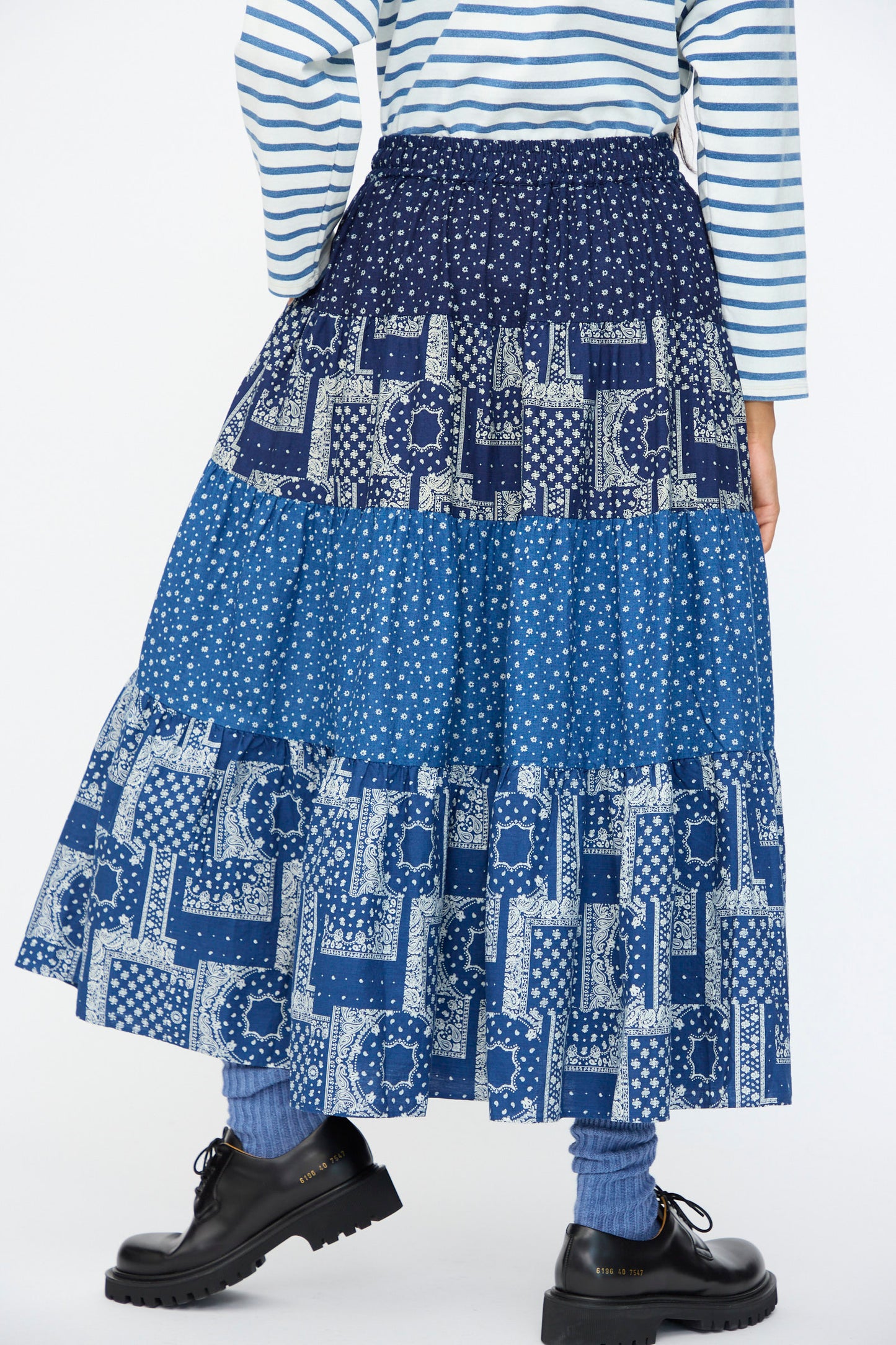 A person wearing a blue and white striped top, the Indigo Flower Skirt in Navy Mix by Ichi Antiquités, blue socks, and black shoes.