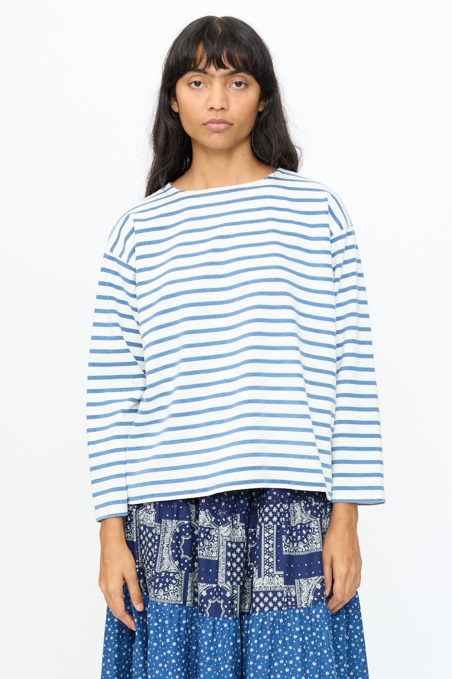 A person with long dark hair wears the Ichi Antiquités Indigo Pullover Tee in White and Blue, paired with a blue patterned skirt, standing against a plain white background.