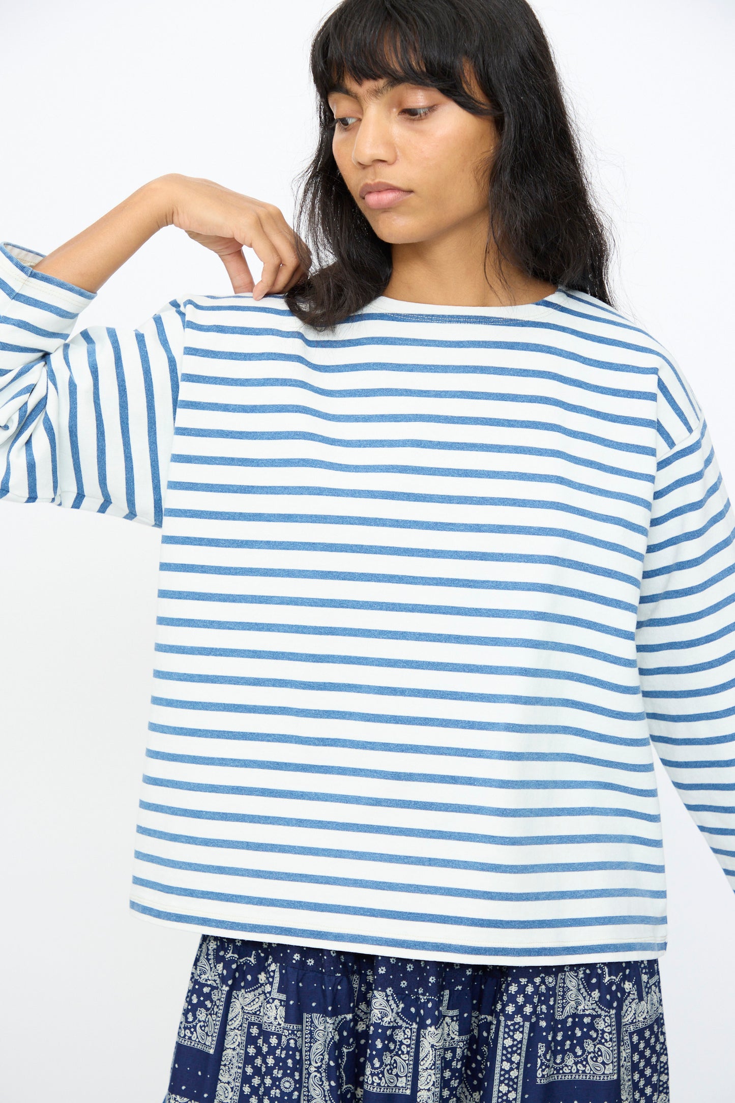 A person wears the Ichi Antiquités Indigo Pullover Tee in White and Blue, paired with a blue patterned skirt, standing against a plain white background.