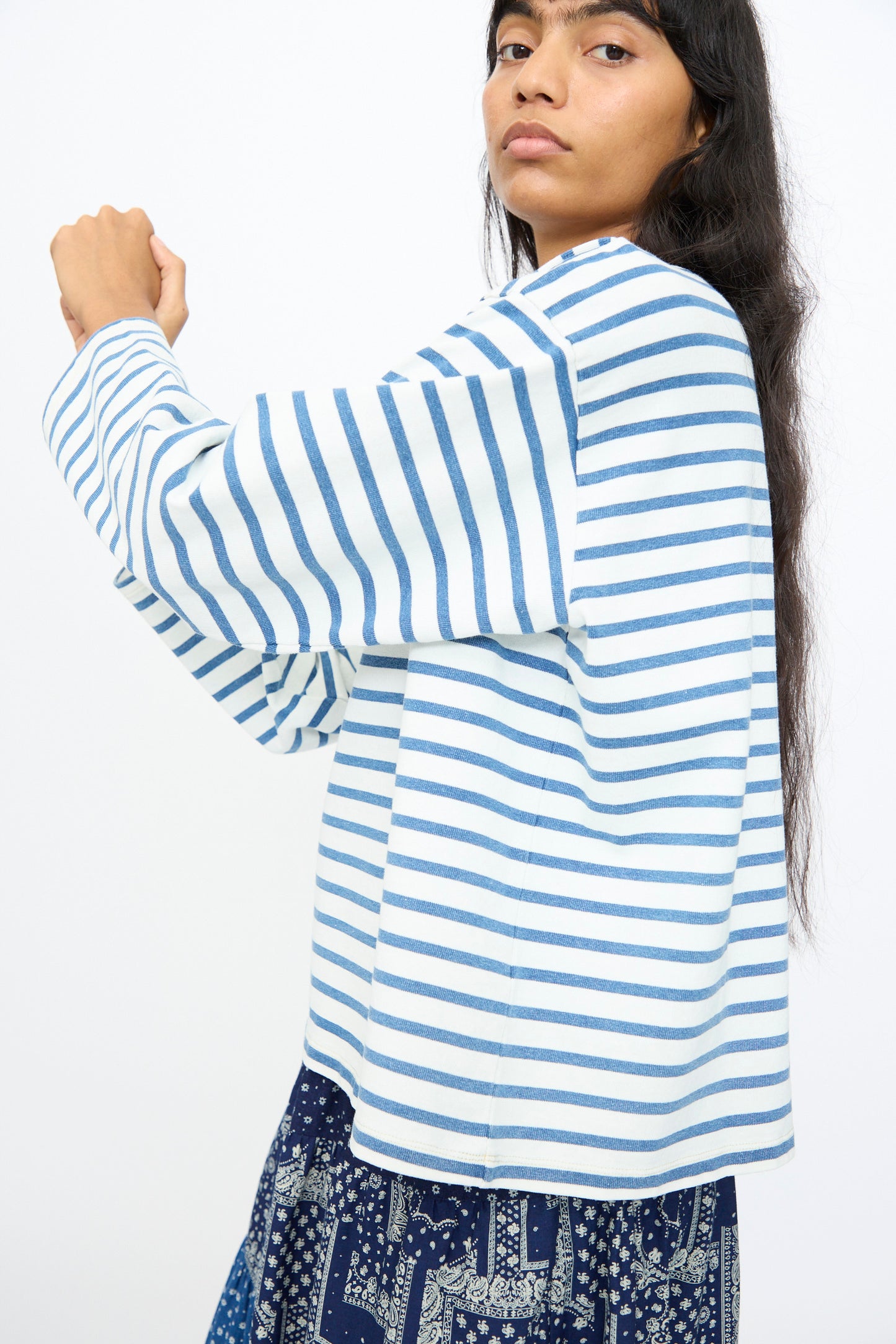 A model wears the Ichi Antiquités Indigo Pullover Tee in White and Blue, paired with a blue patterned skirt, standing against a plain white background.