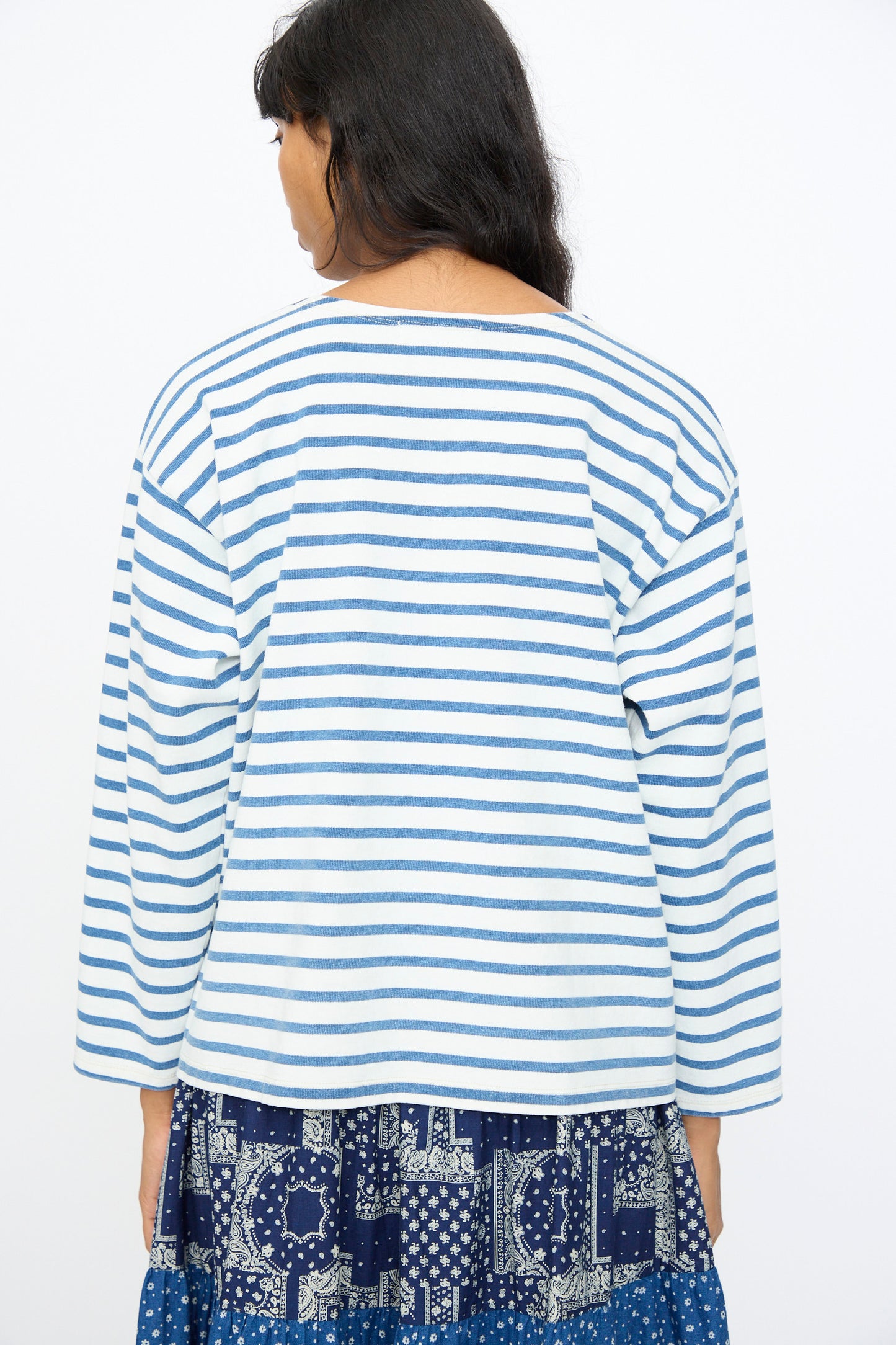 A woman faces away, wearing the Ichi Antiquités Indigo Pullover Tee in White and Blue with a blue patterned skirt, set against a plain white background.