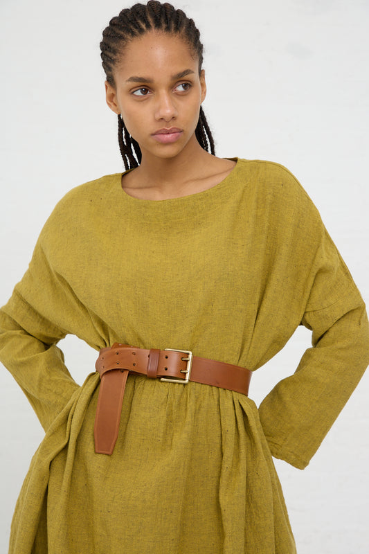 A woman wearing a belted olive green dress with a thoughtful expression, the belt featuring a brass buckle and crafted from cow leather by Ichi Antiquités.