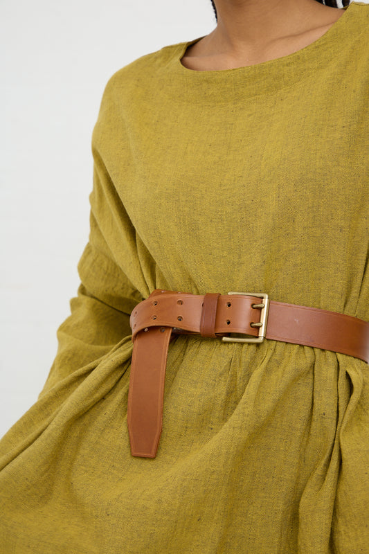A Ichi Antiquités cow leather belt with a brass buckle cinched around a green textured garment.