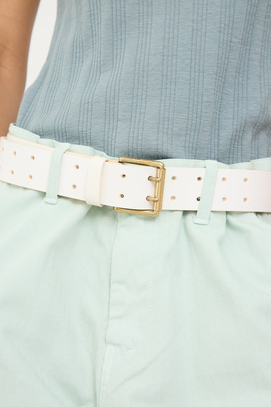 A close-up of a light blue ribbed top tucked into mint green trousers with an Ichi Antiquités cow leather belt in white featuring a brass buckle.