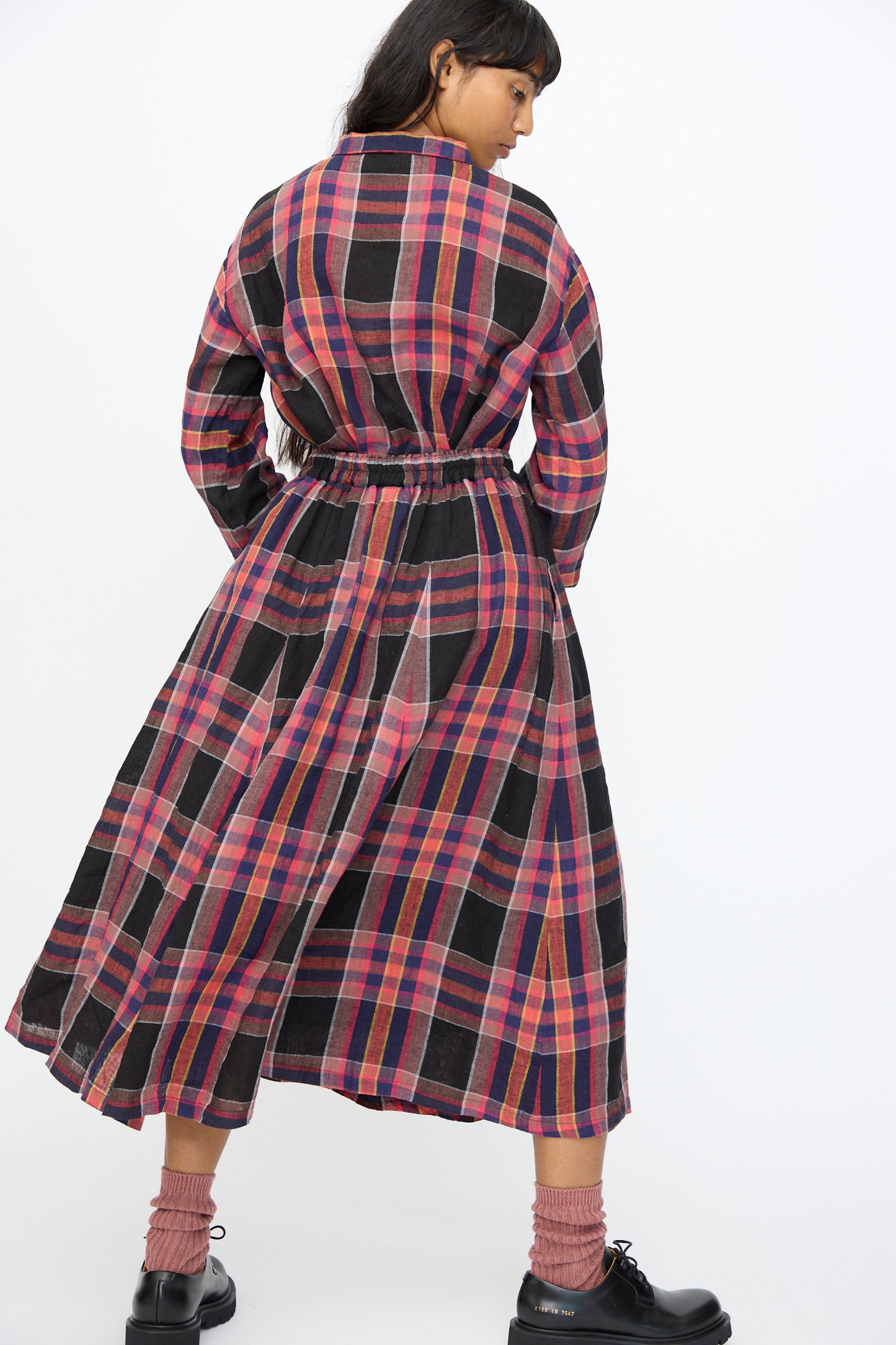 A person stands with their back to the camera, wearing the Ichi Antiquités Linen Check Skirt in Black, styled with black shoes and pink socks.