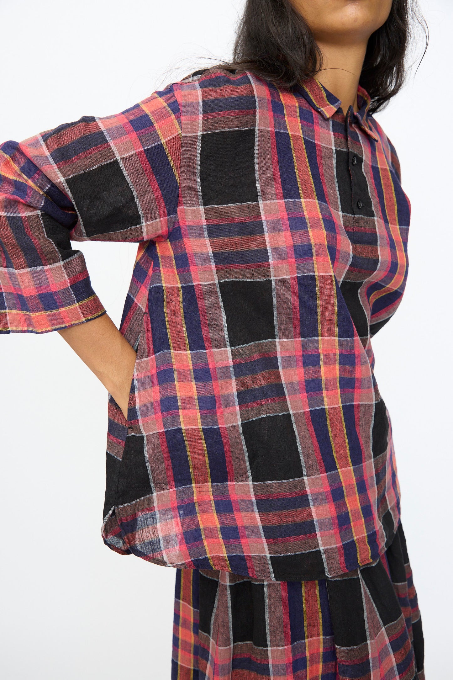 Wearing the Ichi Antiquités Linen Cotton Check Shirt in Black, a person stands with one hand in their pocket, pairing the loose-fit Japanese-made shirt with a matching skirt.