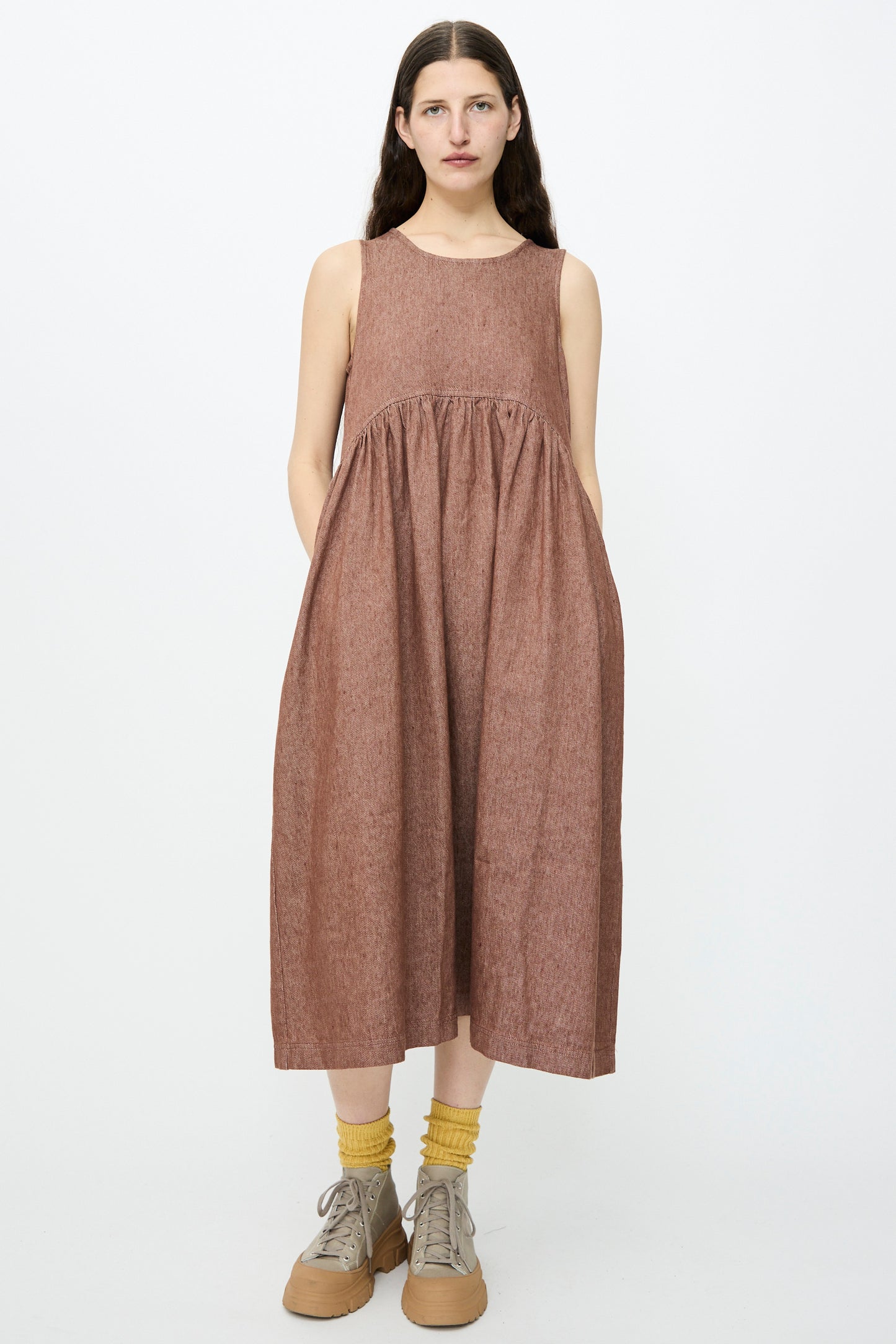 A person in an Ichi Antiquités Linen Cotton Denim Dress in brown, styled with yellow socks and beige shoes, stands against a plain white background.