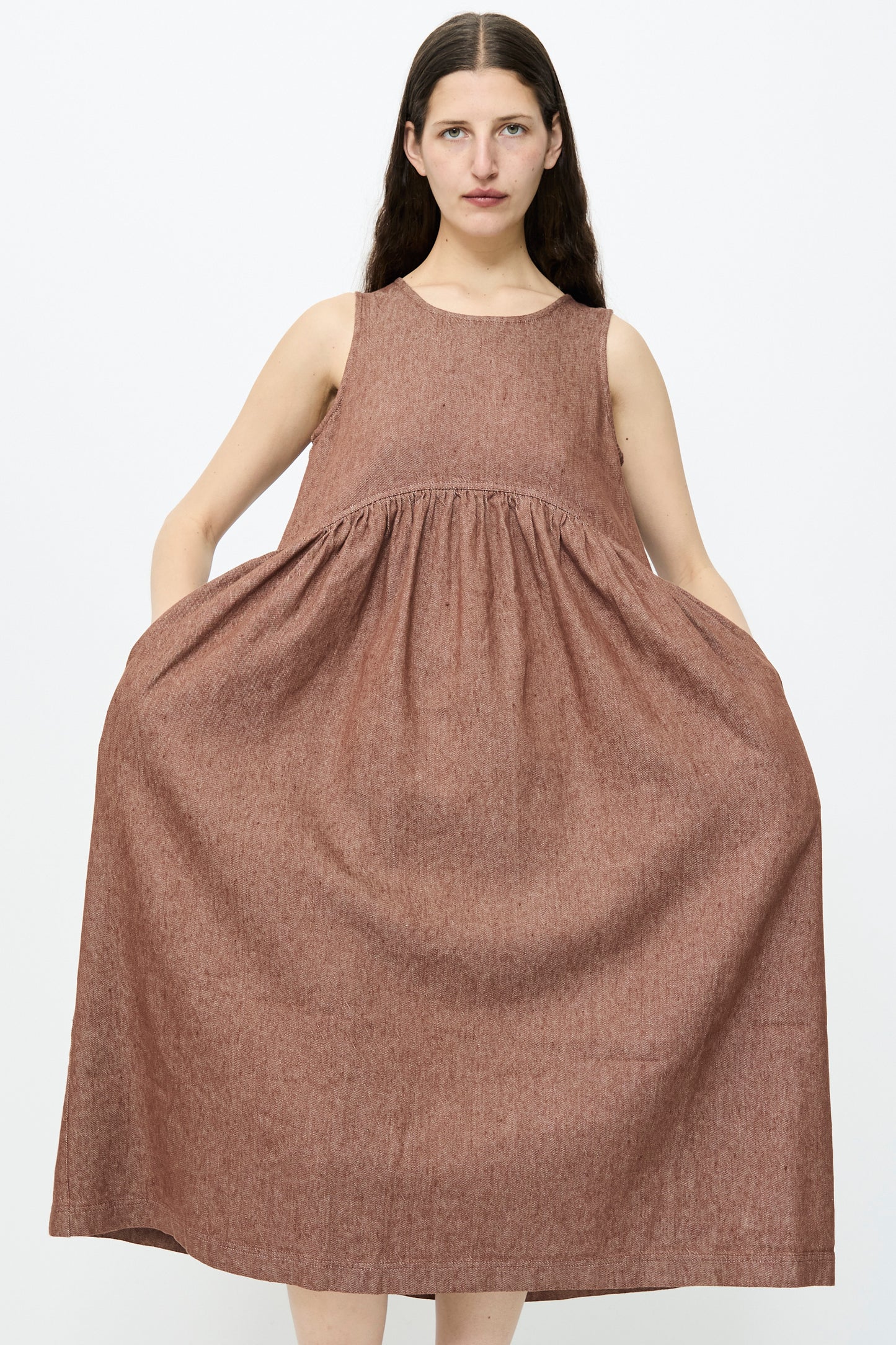 Someone wearing the Ichi Antiquités Linen Cotton Denim Dress in Brown, a relaxed fit sleeveless dress with pockets, stands against a plain background.