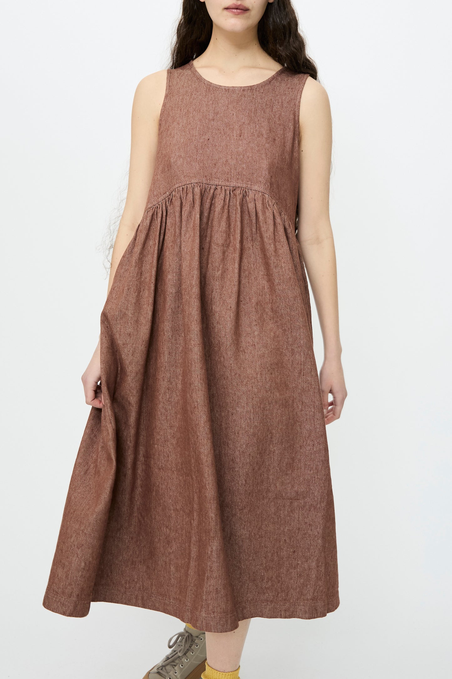 A woman poses against a plain background, highlighting the Linen Cotton Denim Dress in Brown by Ichi Antiquités. The sleeveless, knee-length dress has a relaxed fit.