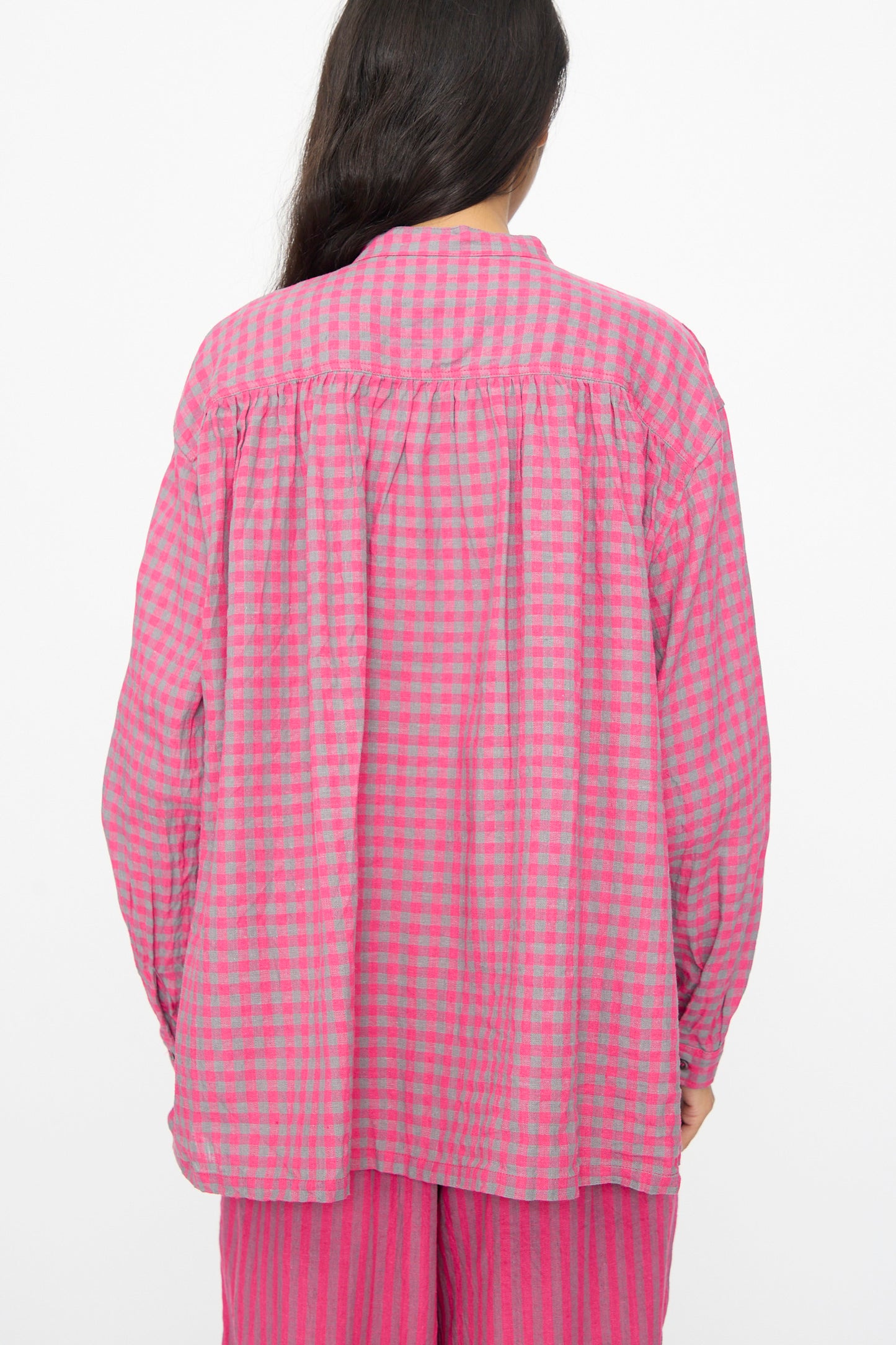 A person with long dark hair is seen from the back, wearing the Ichi Antiquités Linen Cotton Gingham Check Shirt in Pink—a loose-fitting, band-collared top crafted in a comfy linen cotton blend.