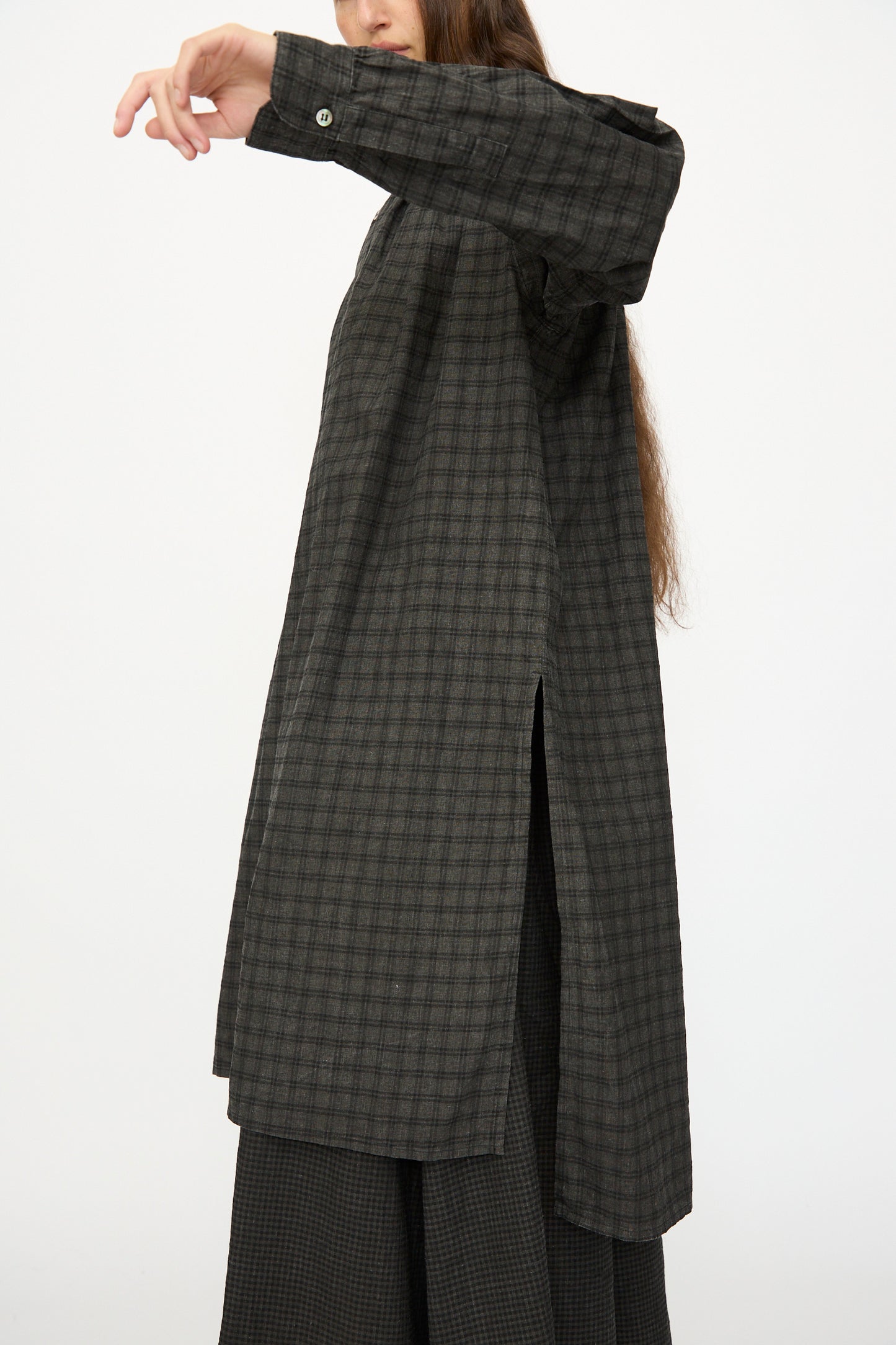 Person wearing the Ichi Antiquités Linen Cotton Gingham Sumi Shirt in Pin Check, oversized with side slits, styled with matching wide-leg pants. Dark plaid pattern, arm raised, face partially out of frame against a plain white background.