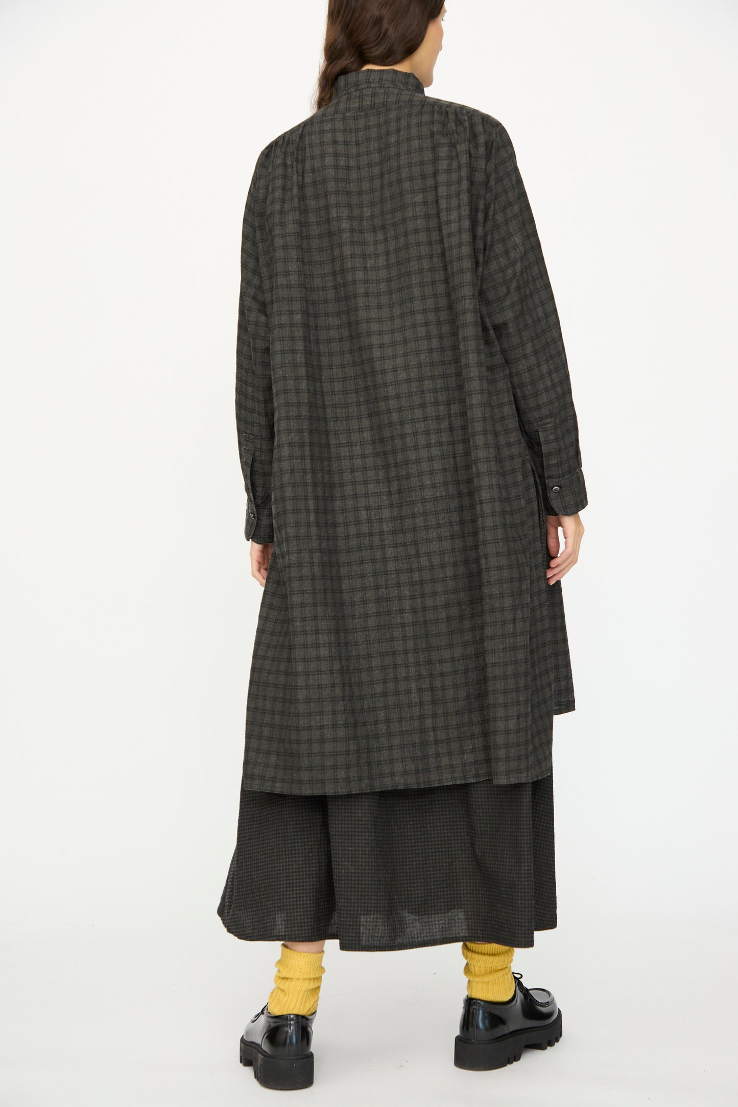 A person faces away, wearing the Ichi Antiquités Linen Cotton Gingham Sumi Shirt in Pin Check, paired with a black skirt, yellow socks, and black shoes, set against a plain white background.