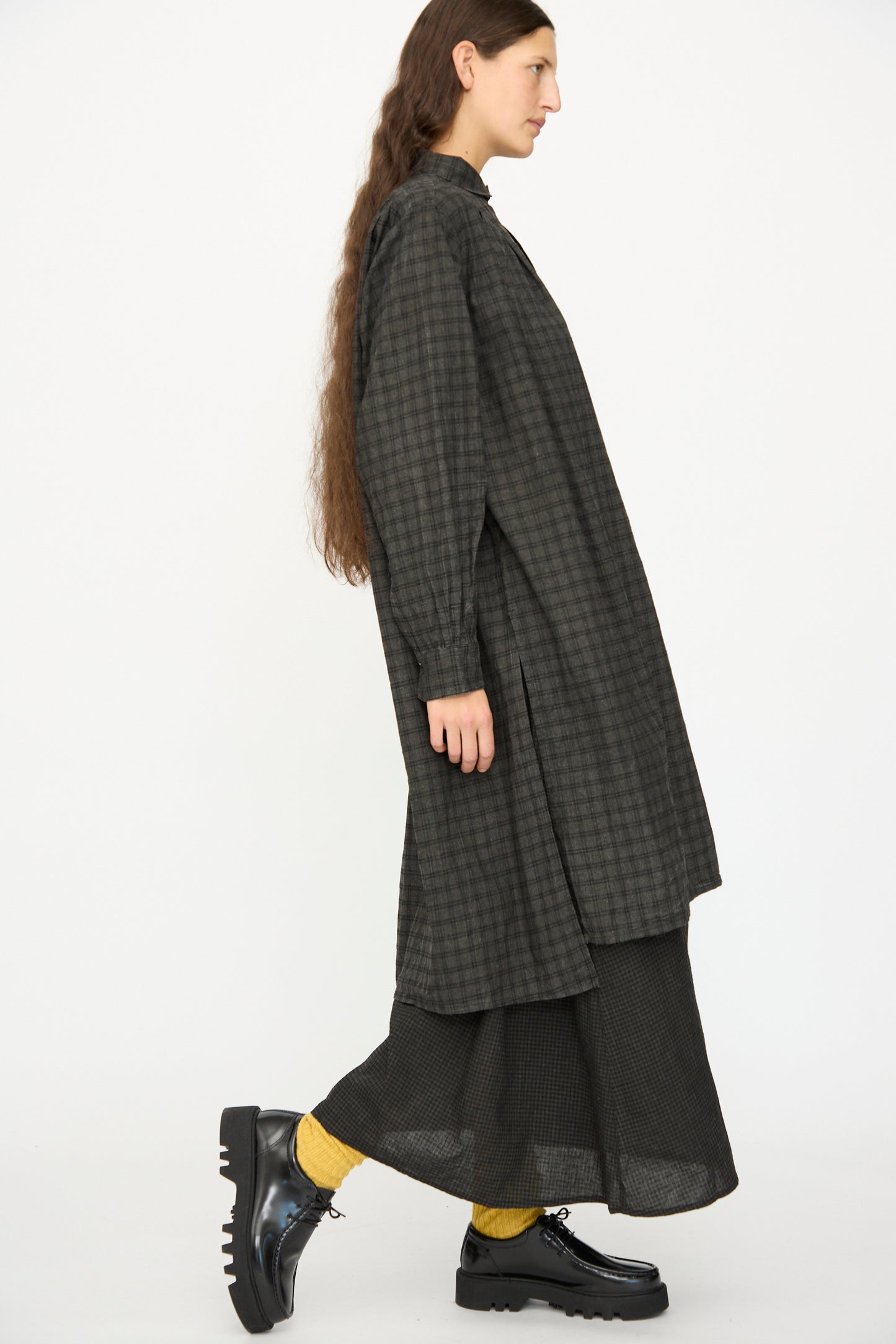 A person with long brown hair wears the Ichi Antiquités Linen Cotton Gingham Sumi Shirt in Pin Check over a black skirt, yellow socks, and black platform shoes, standing in profile against a white background.