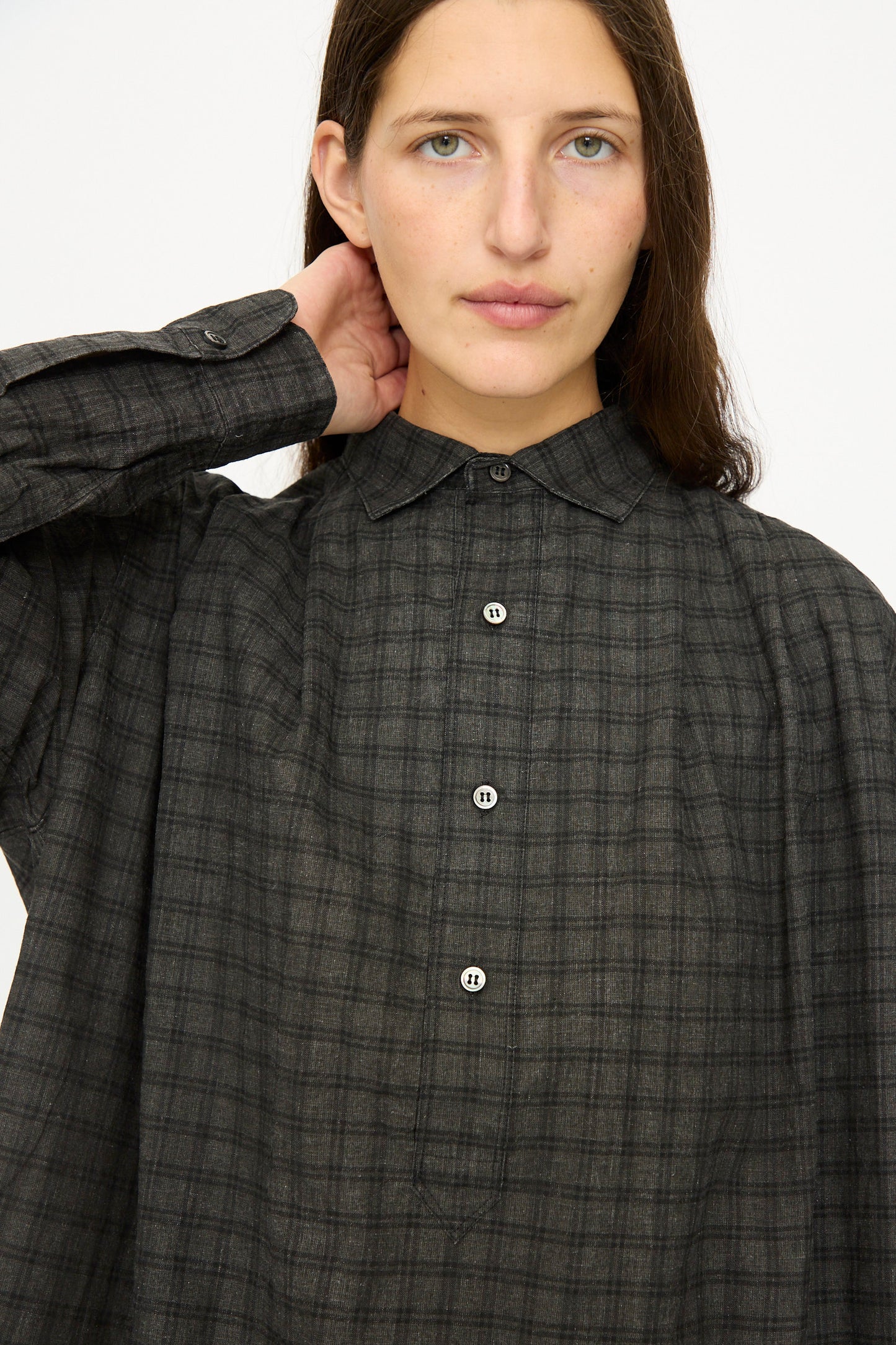 A person with long brown hair wears the Ichi Antiquités Linen Cotton Gingham Sumi Shirt in Pin Check, an oversized long-sleeve shirt, standing against a plain white background.