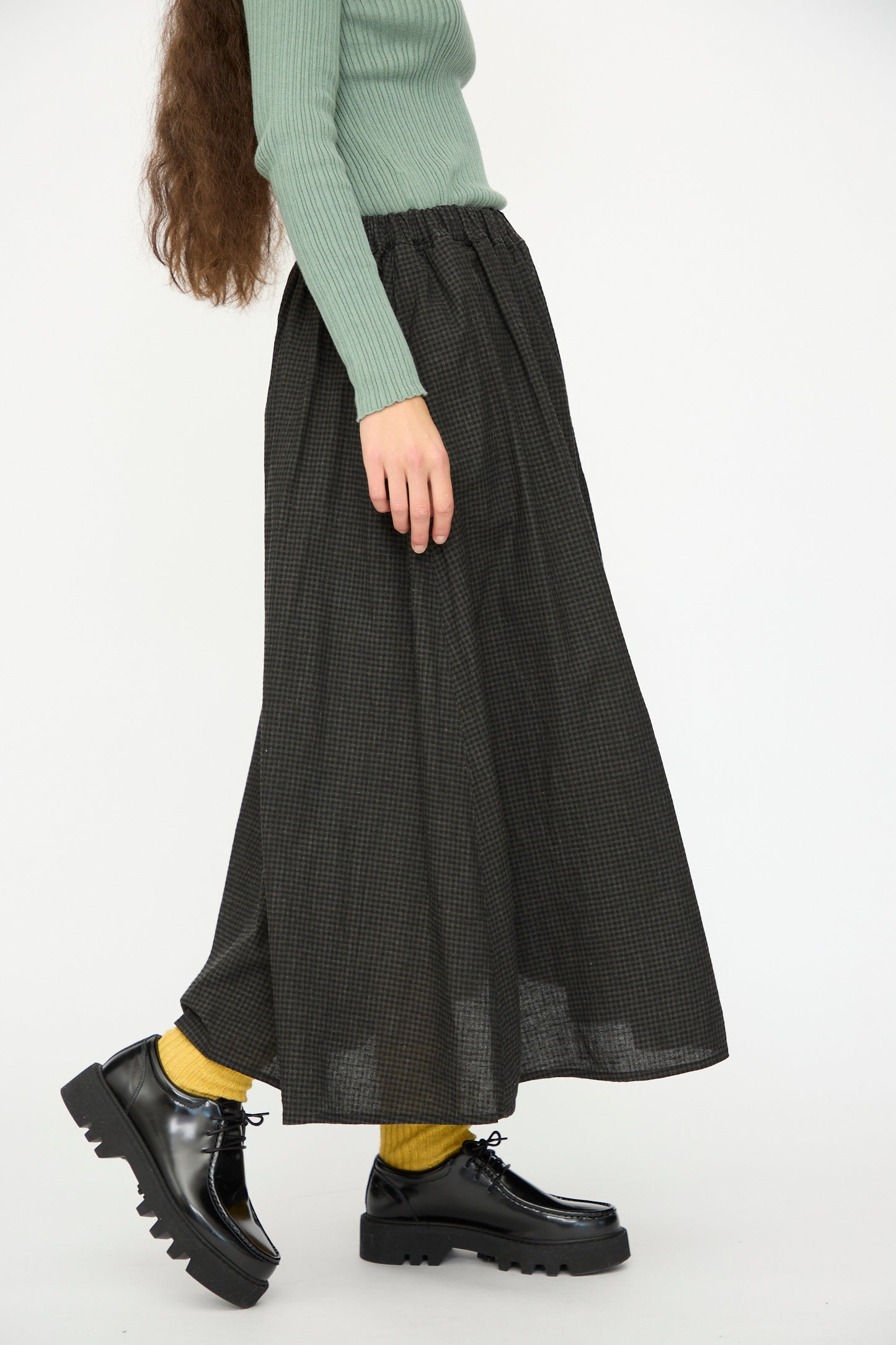 A person wears a green ribbed sweater, yellow socks, black platform shoes, and the Ichi Antiquités Linen Cotton Gingham Sumi Skirt in Check, standing against a white background.