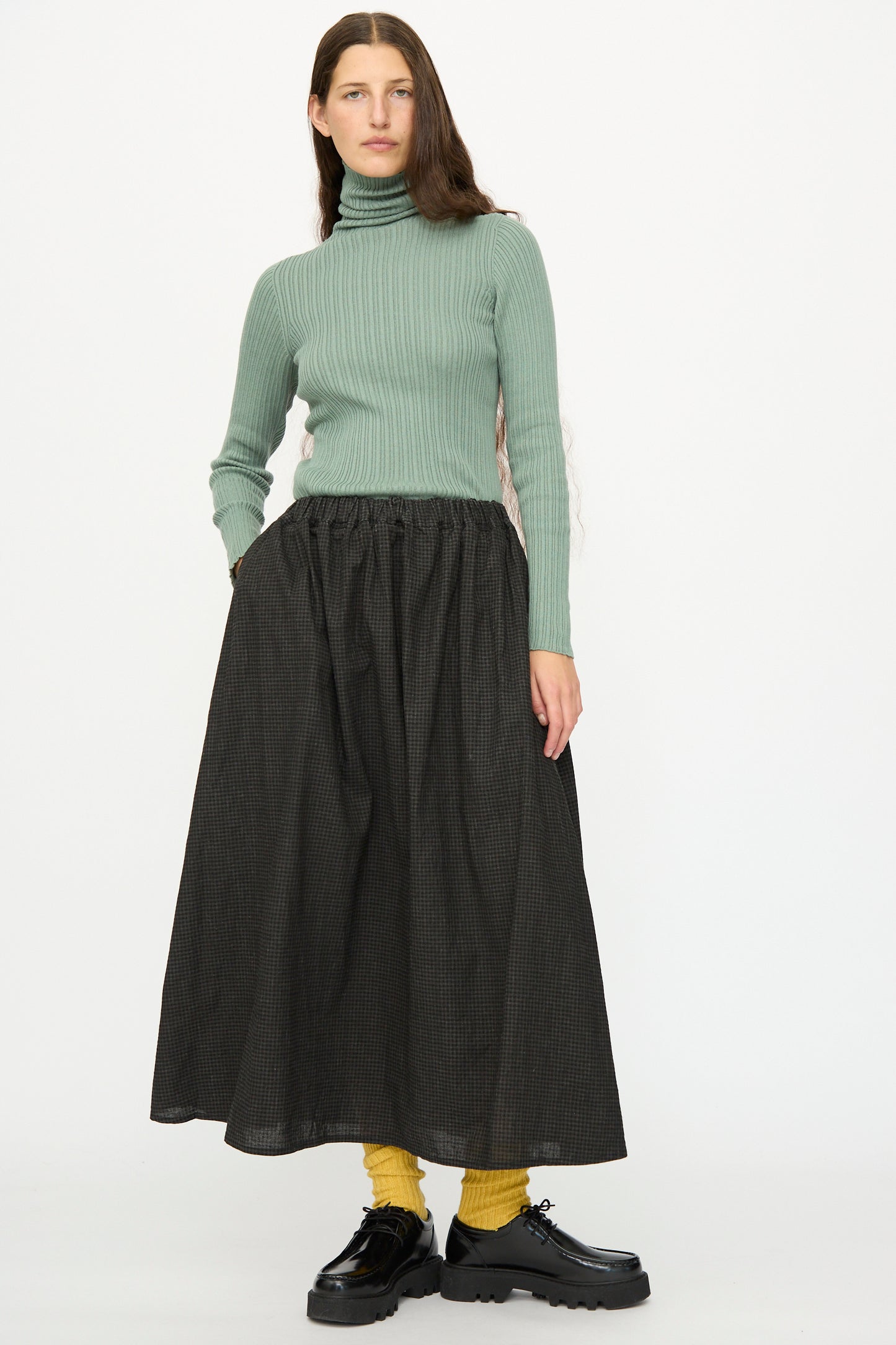 A person wearing a light green ribbed turtleneck, yellow socks, black platform shoes, and the Ichi Antiquités Linen Cotton Gingham Sumi Skirt in Check stands against a plain white background.