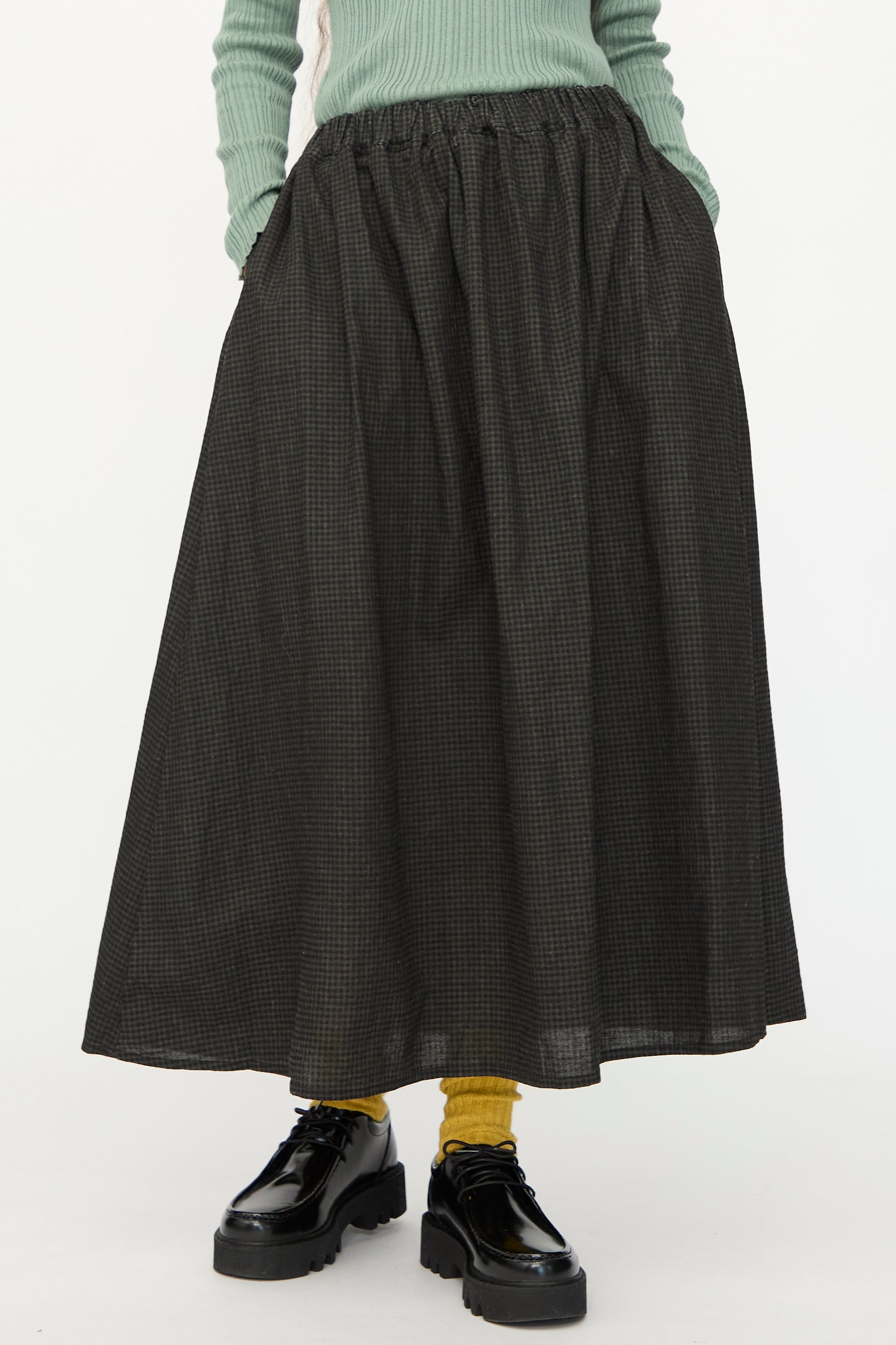 A person wears a light green ribbed sweater, yellow socks, black platform shoes, and the Ichi Antiquités Linen Cotton Gingham Sumi Skirt in Check, standing against a plain background.