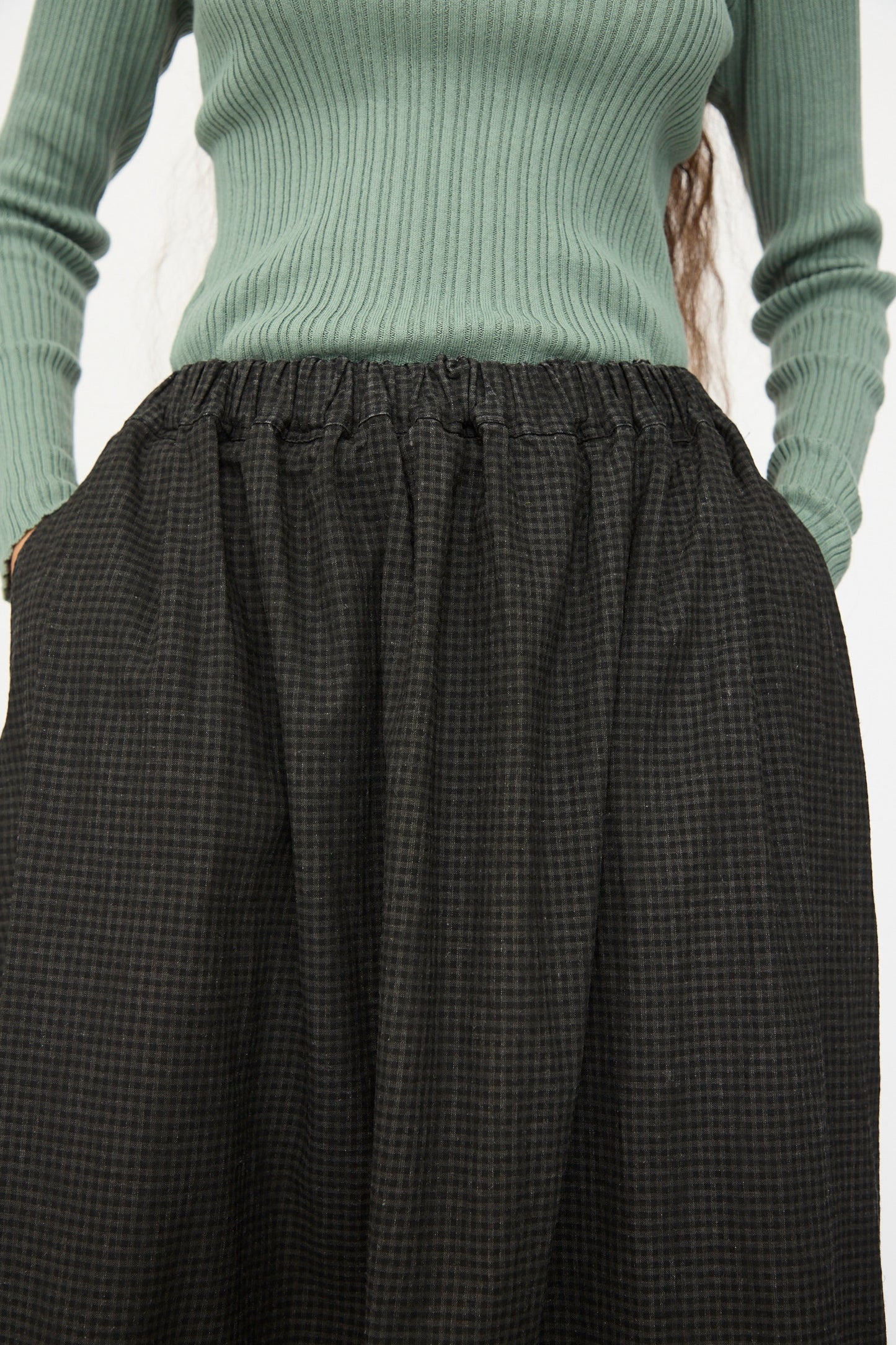 A person wearing a ribbed, long-sleeve green top and the Ichi Antiquités Linen Cotton Gingham Sumi Skirt in Check, styled high-waisted and A-line with hands in the skirt pockets.