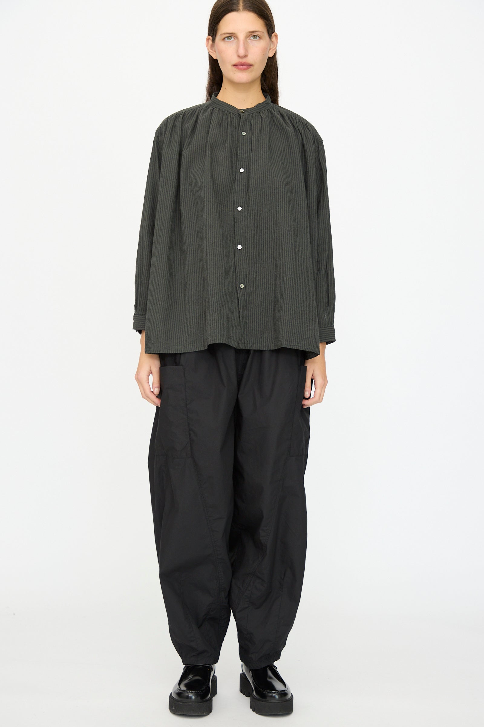 A person faces forward against a white background wearing the Ichi Antiquités Linen and Cotton Stripe Shirt in Charcoal, paired with wide black pants and black shoes.
