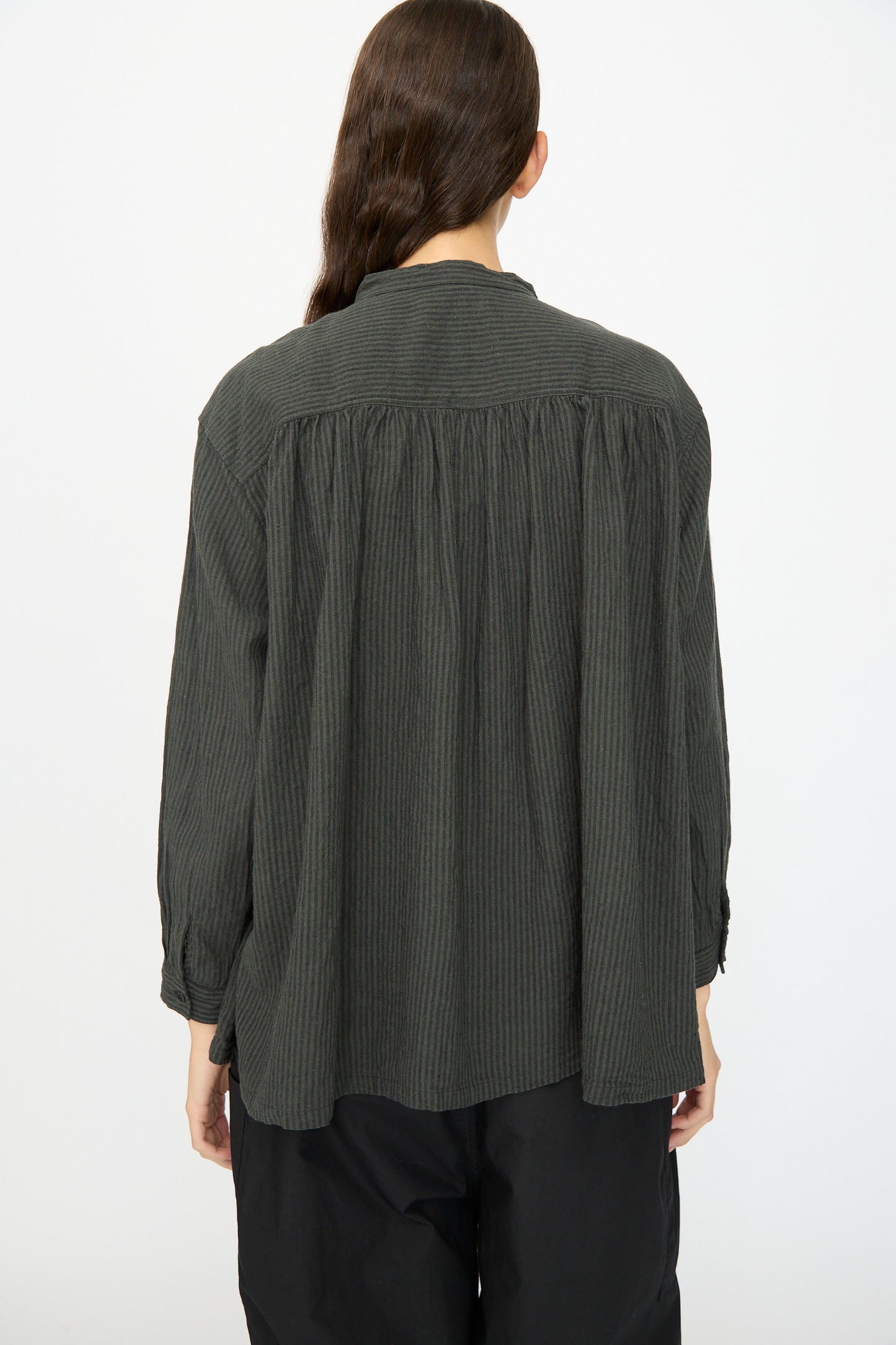 Person with long brown hair wearing the Ichi Antiquités Linen and Cotton Stripe Shirt in Charcoal, shown from the back against a plain light background, paired with black pants.