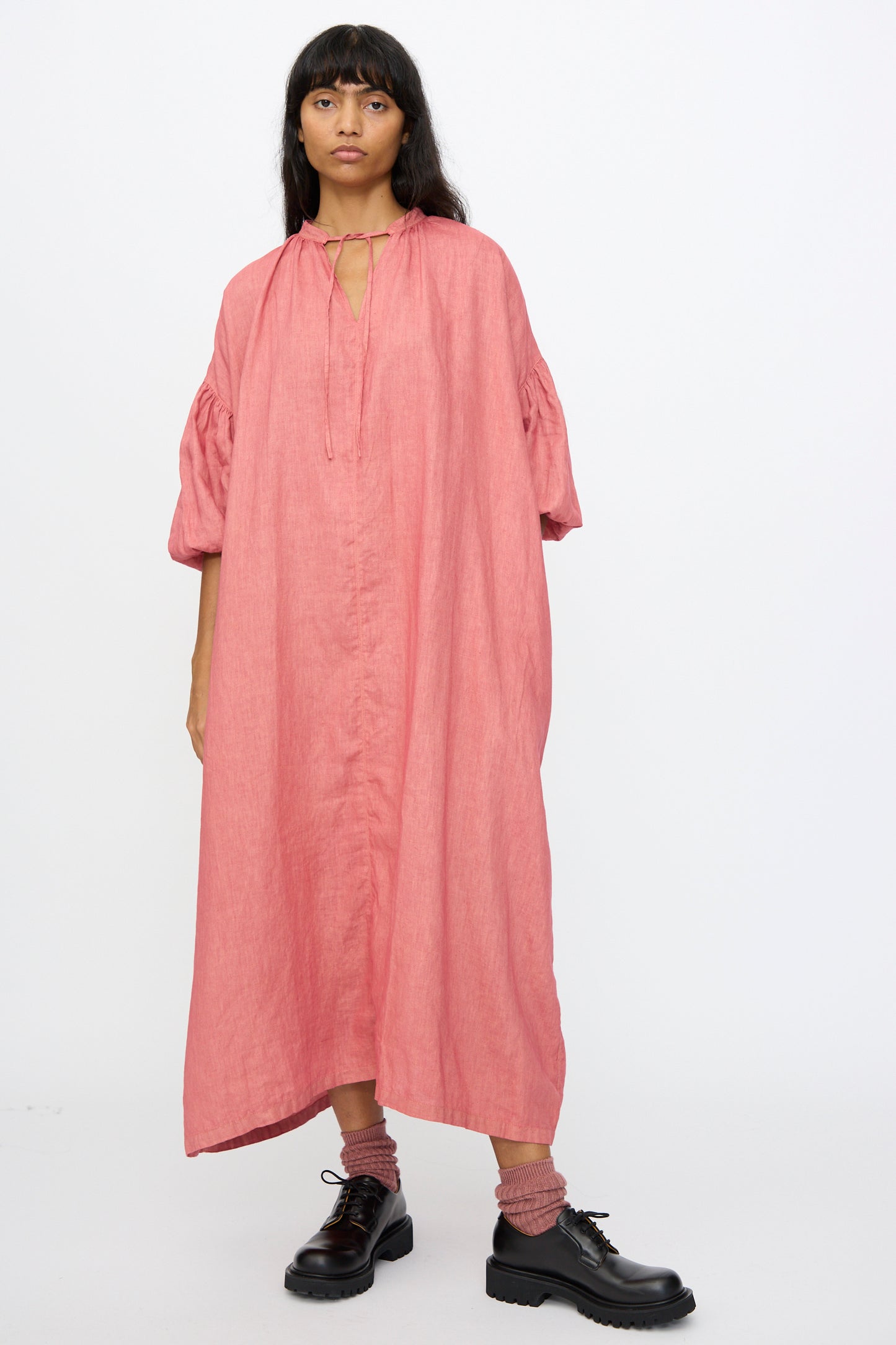 A person wearing the Ichi Antiquités Linen Dress in Pink, styled with pink socks and black lace-up shoes, stands against a plain white background.