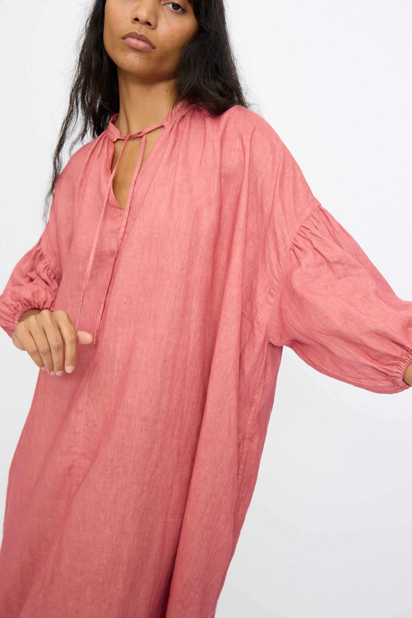 A person wears the Ichi Antiquités Linen Dress in Pink, a loose-fitting, hand-dyed linen maxi dress with a gathered neckline and ties, posing against a plain light background.