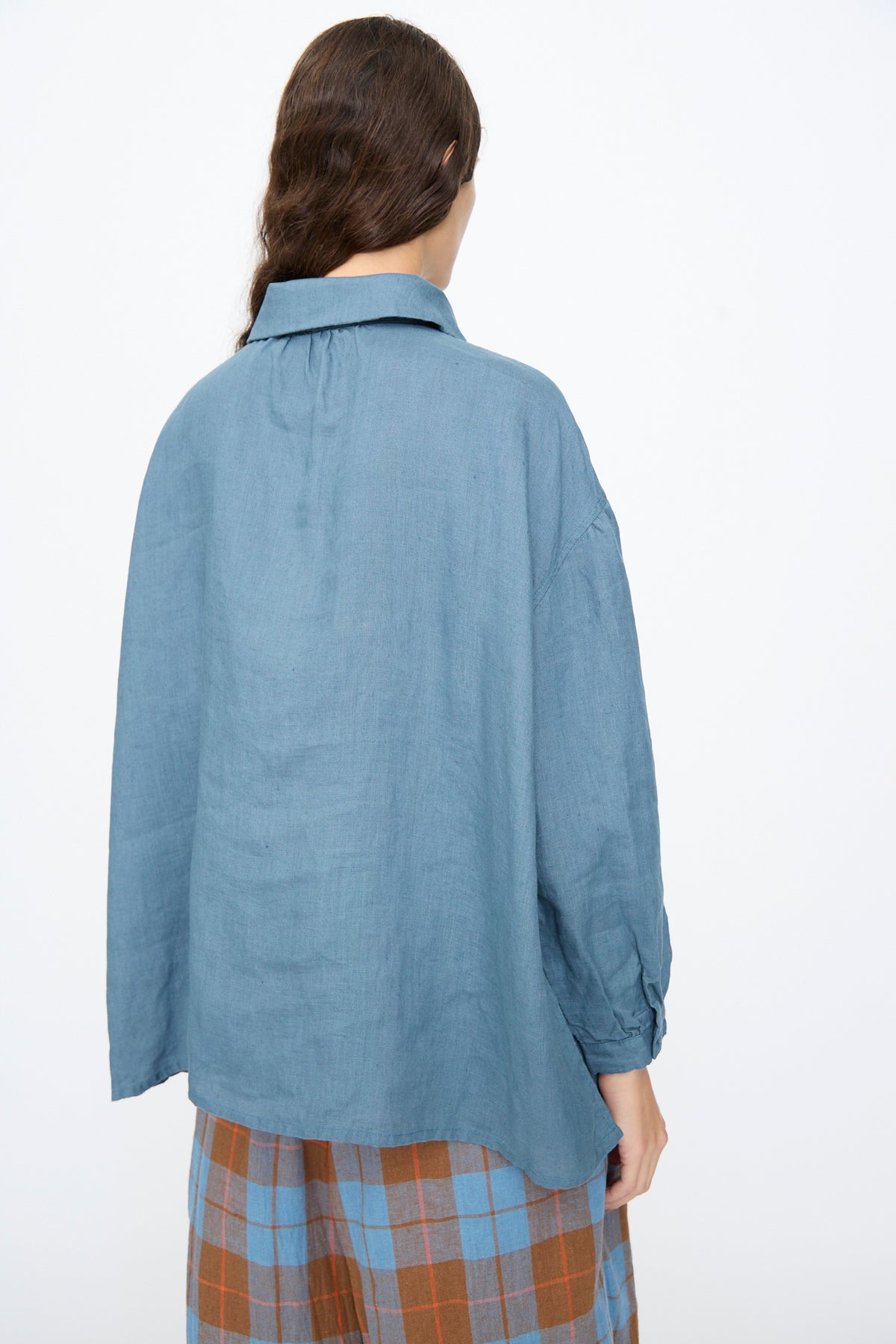 Back view of a person wearing a blue Linen Shirt in Earth Blue and plaid pants.