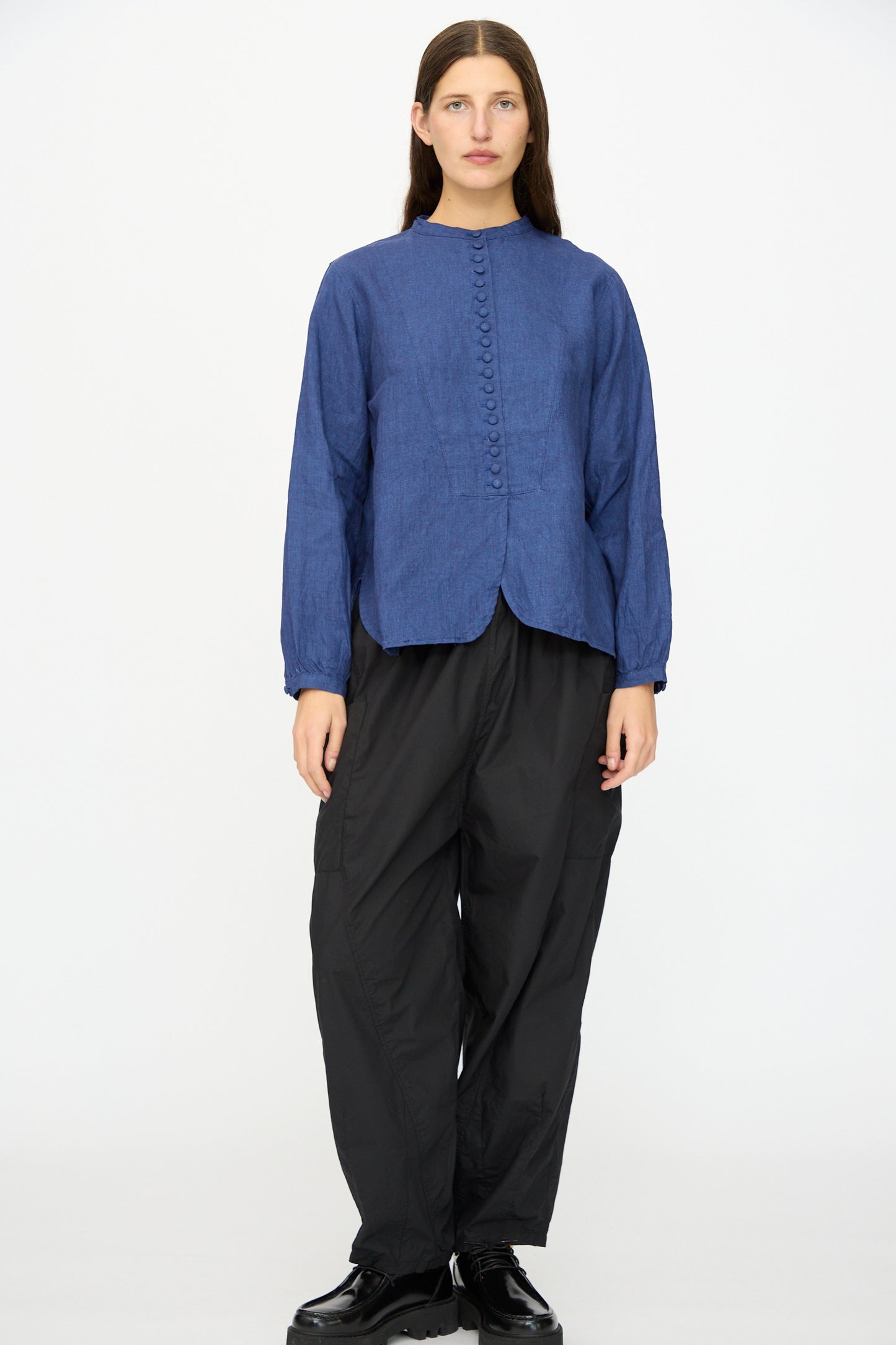 A person stands against a plain background wearing the Ichi Antiquités Linen Shirt in Indigo, paired with loose black pants and black shoes.