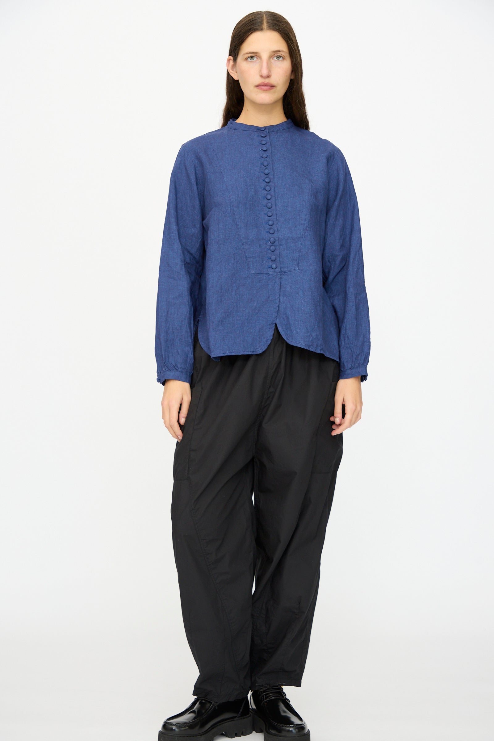 A person stands against a plain background wearing the Ichi Antiquités Linen Shirt in Indigo, paired with loose black pants and black shoes.