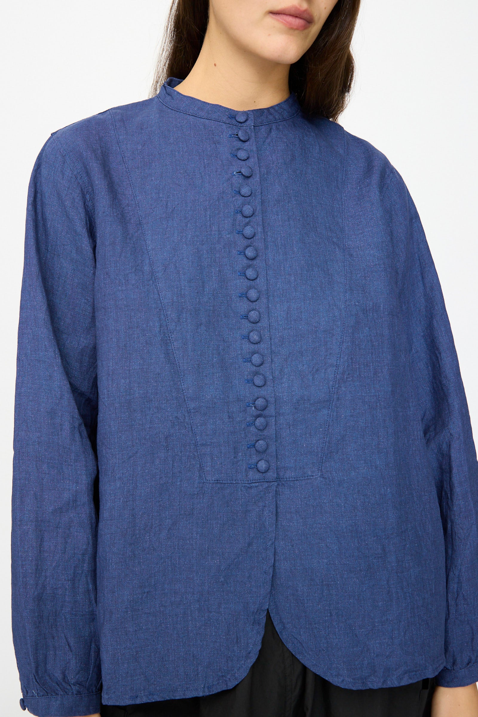 A woman wears the Ichi Antiquités Linen Shirt in Indigo, featuring long sleeves, a band collar, and a scalloped hem, made in Japan.
