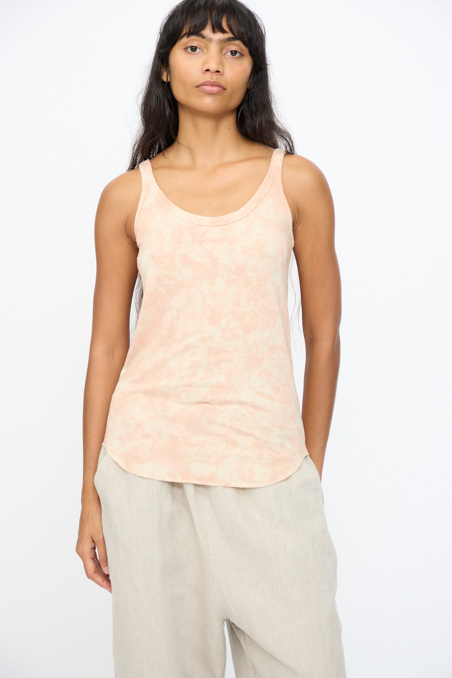 A person stands facing forward, wearing the Ichi Antiquités Silk Jersey Tie Dye Tank in Light Pink Mahogany and beige pants against a plain white background.