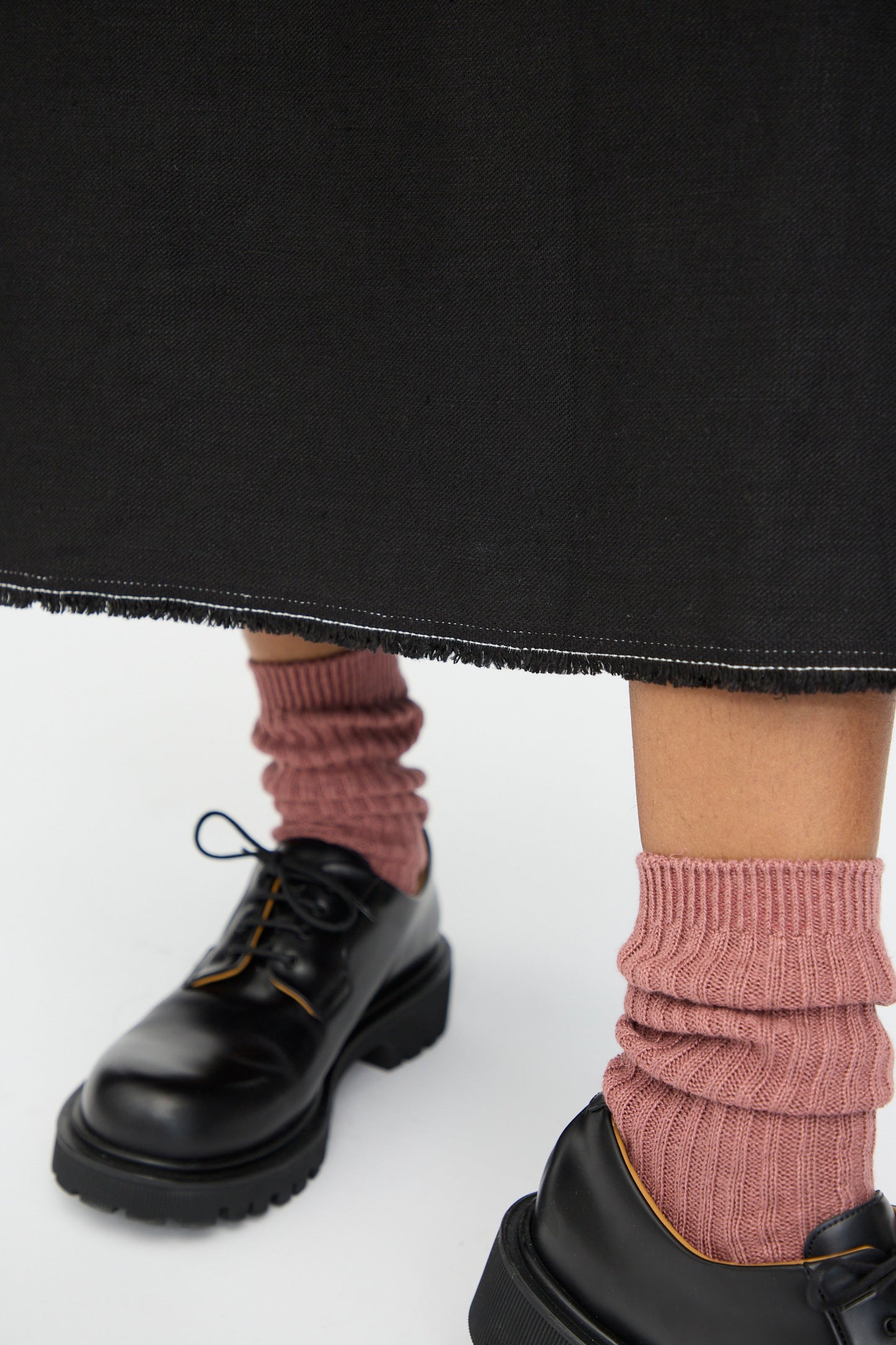 A person wears the Ichi Antiquités Twill Weave Linen Dress in Black with pink ribbed socks and black lace-up shoes, standing on a white background.
