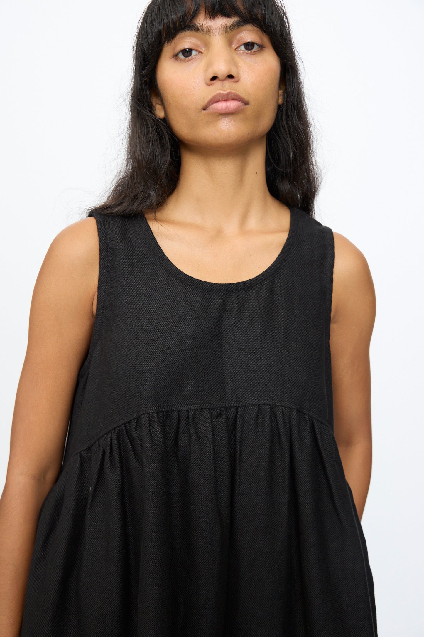 A woman with long dark hair wears the Ichi Antiquités Twill Weave Linen Dress in Black, sleeveless and maxi-length, standing against a plain white background.