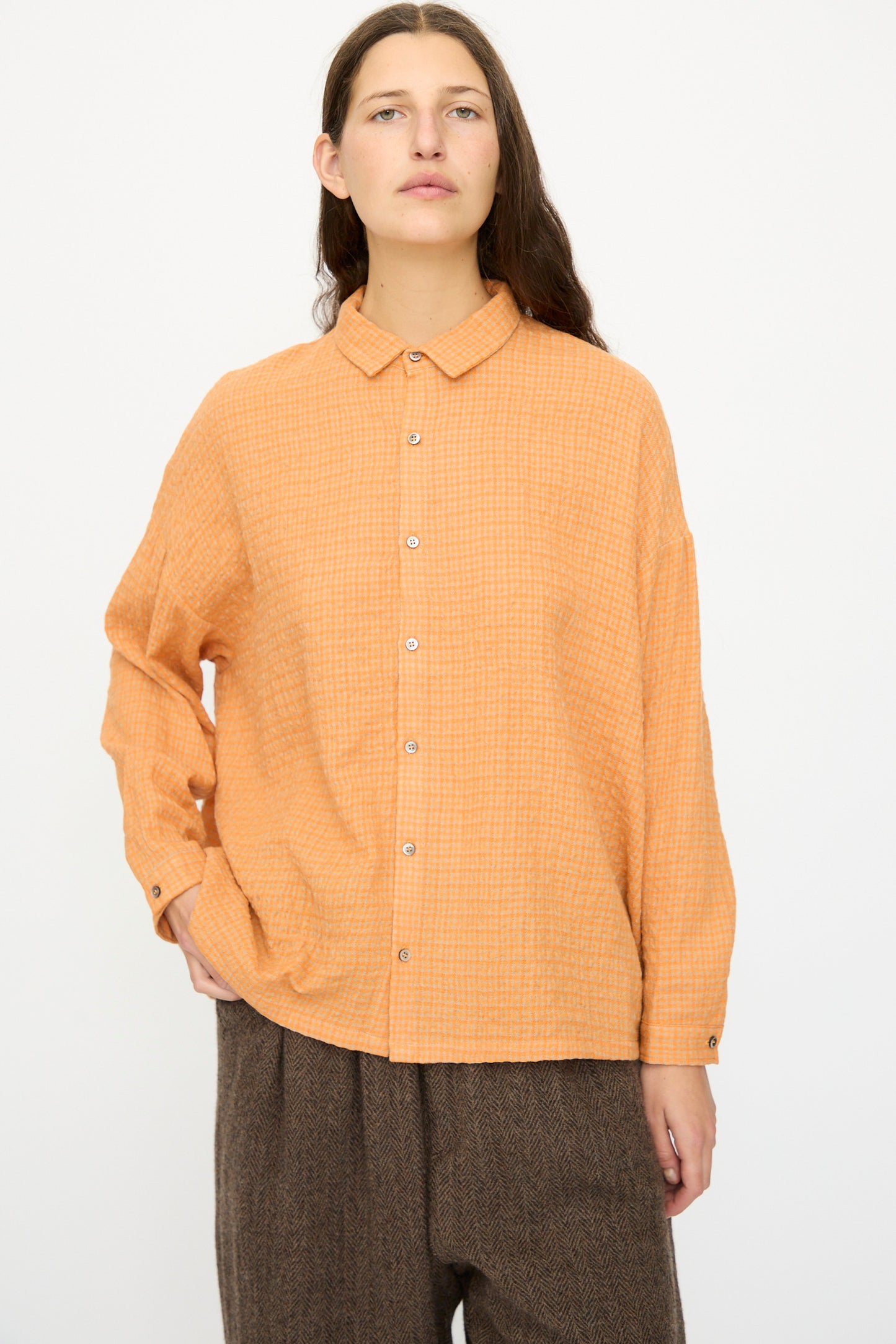 A person wears the Ichi Antiquités Wool Cotton Gingham Shirt in Orange and Mocha with brown loose-fitting pants, standing against a plain white background.