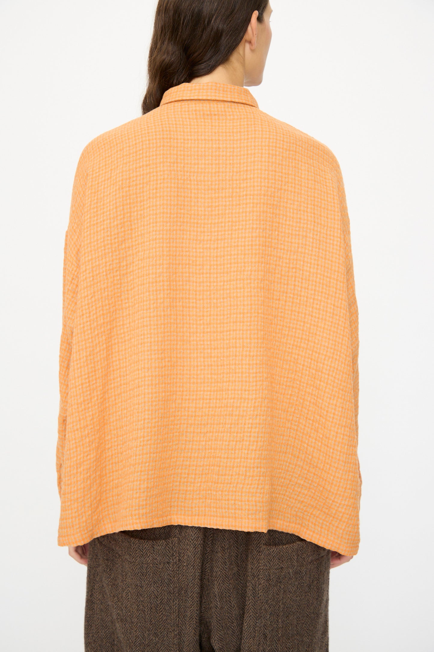 A person stands with their back to the camera, wearing the Ichi Antiquités Wool Cotton Gingham Shirt in Orange and Mocha, paired with brown pants, against a plain background.