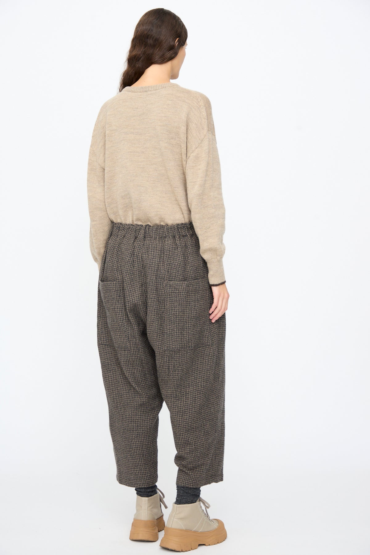 A person viewed from behind wearing a tan sweater, Ichi Antiquités Wool Gauze Houndstooth Pants in Mocha, and light tan lace-up boots.