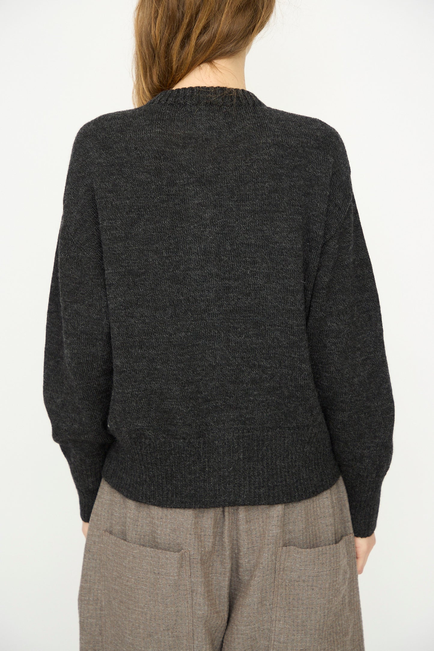 A person faces away from the camera, wearing the Ichi Antiquités Wool Knit Cardigan in Black and loose brown pants, set against a plain light background.