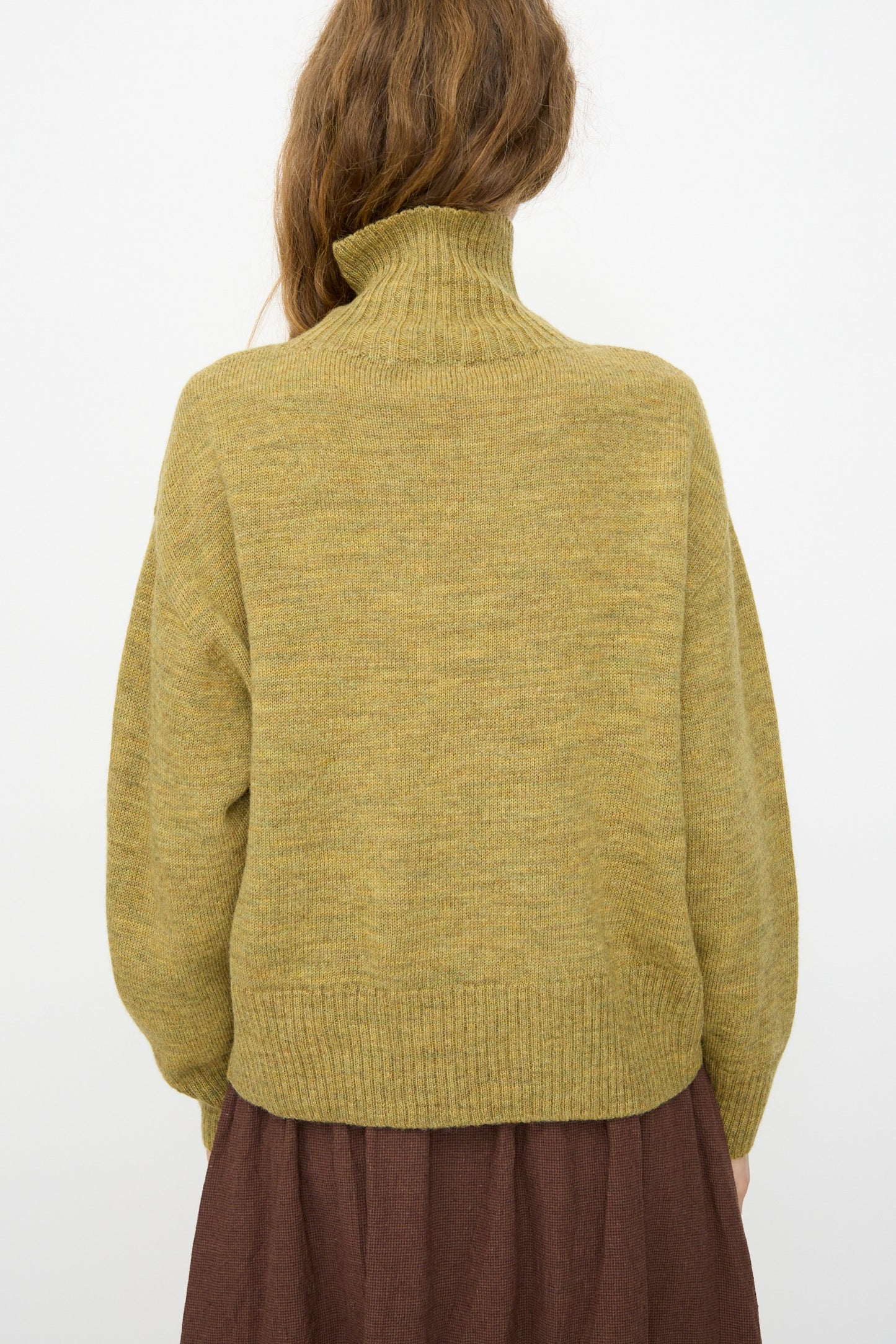 A person with long brown hair wears the Ichi Antiquités Wool Whole Garment Knit Pullover in Mustard and a brown skirt, shown from the back against a plain background.