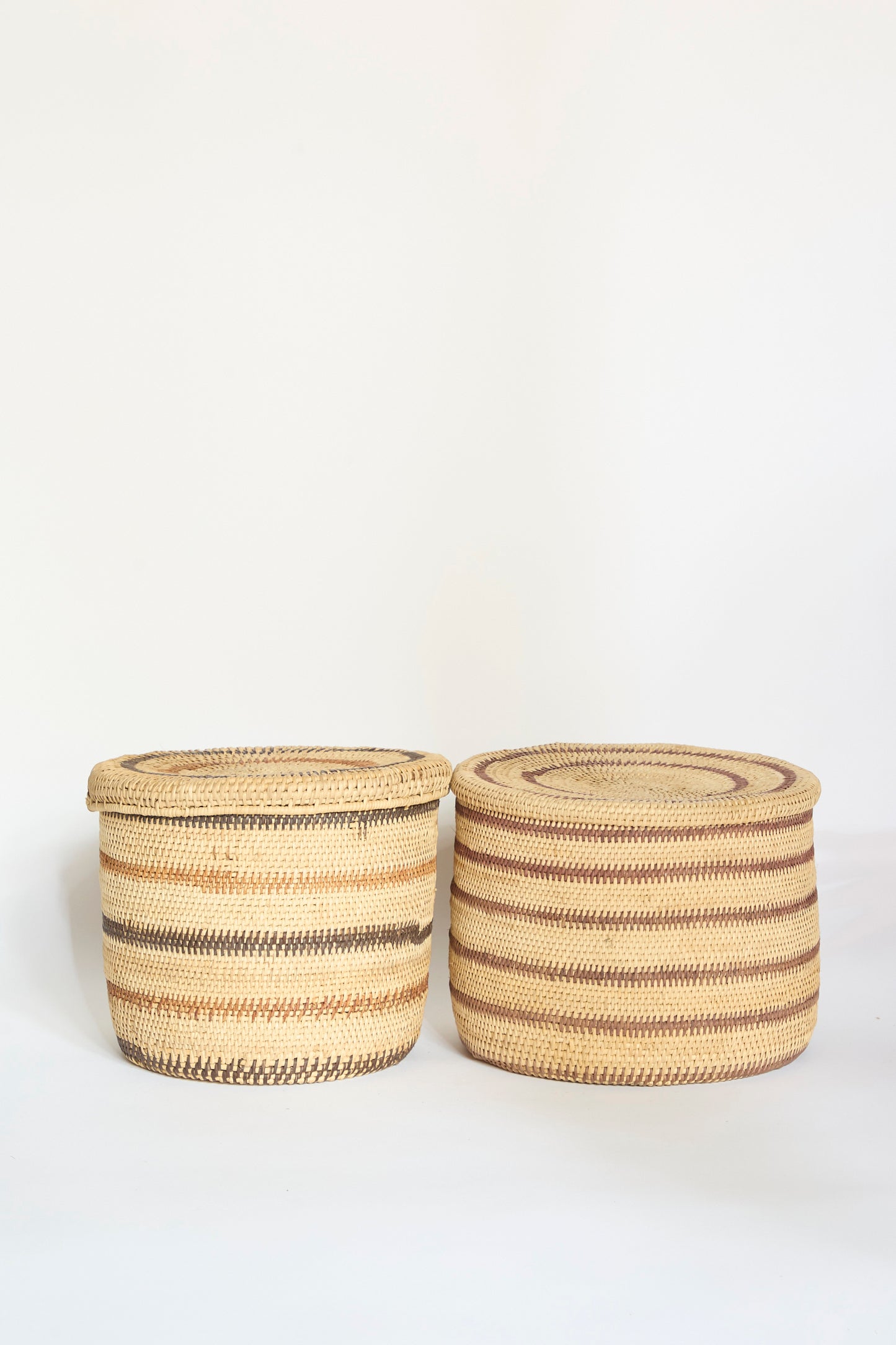 Two round Motorohina Baskets with Yanomami Stripe Painting Mixed from Incausa—each a beautiful handwoven Amazon basket—feature brown, tan, and beige horizontal stripes, sitting side by side against a plain white background.