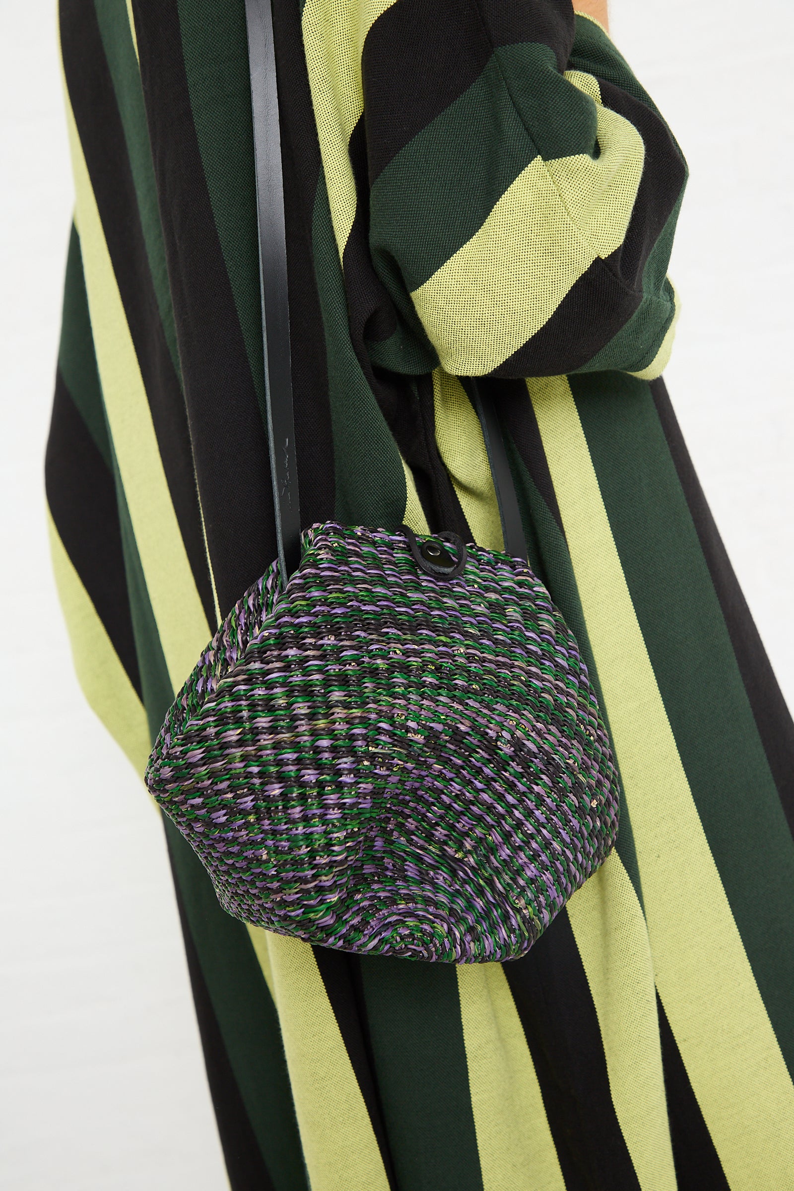A person wearing a black and green striped dress with an Inès Bressand N. 14 Mini Shell Bag in Green.