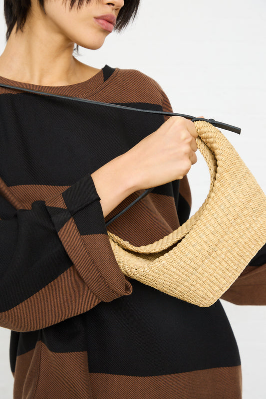 Woman in a striped top holding a handwoven Inès Bressand N. 35 Mini Croissant Bag in Natural.