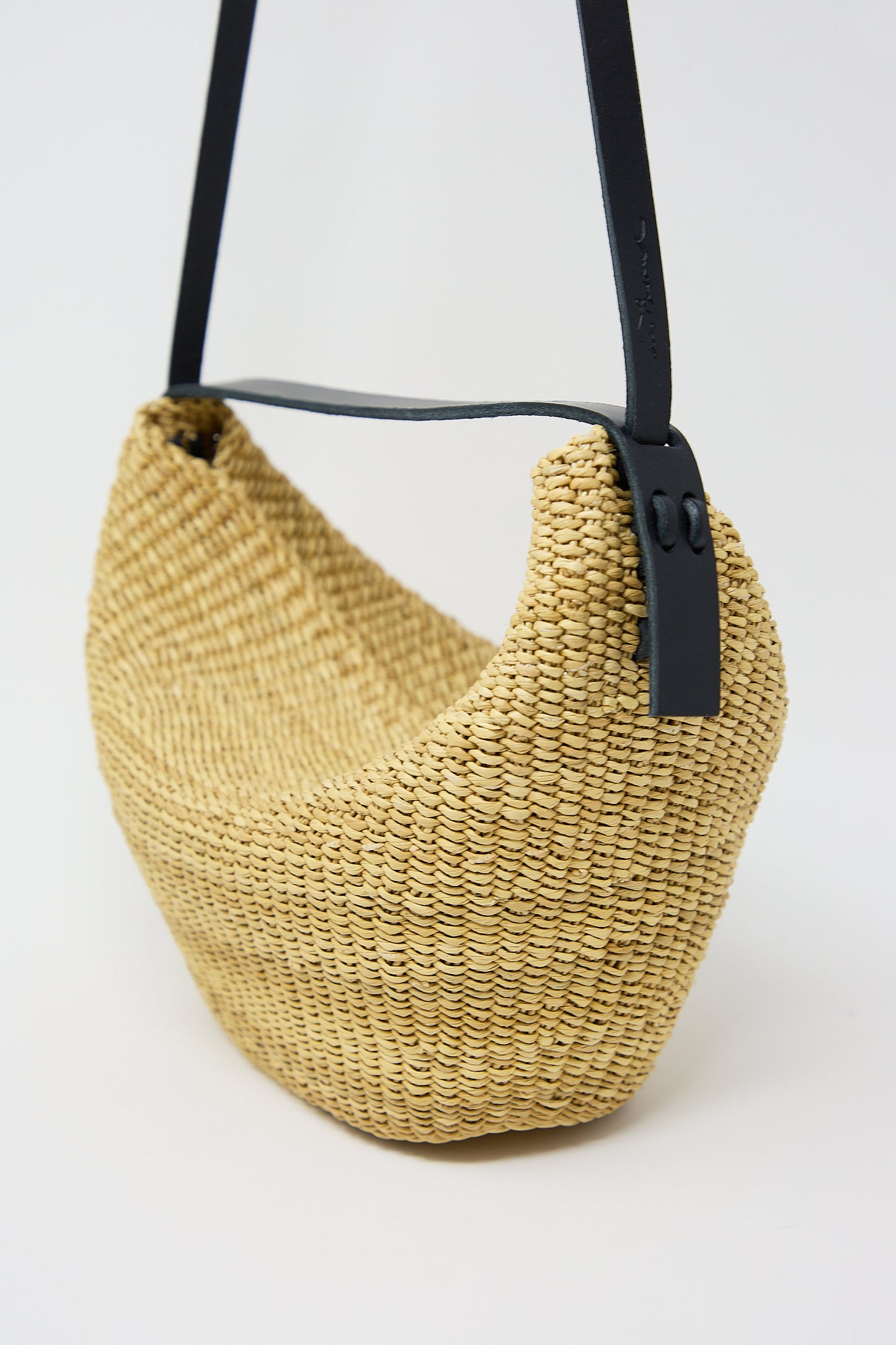 Handwoven beige N. 35 Mini Croissant Bag in Natural with black strap on a white background by Inès Bressand.