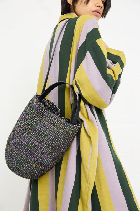 A person wearing a striped garment and carrying an Inès Bressand N. 36 Haricot Bag in Green with vegetable-tanned leather handles.
