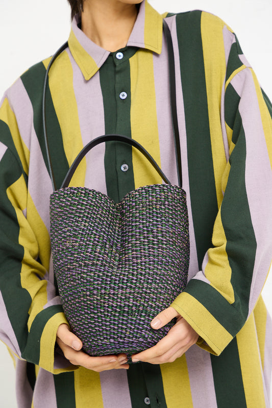 Person holding an Inès Bressand N. 36 Haricot Bag in Green against a striped shirt.