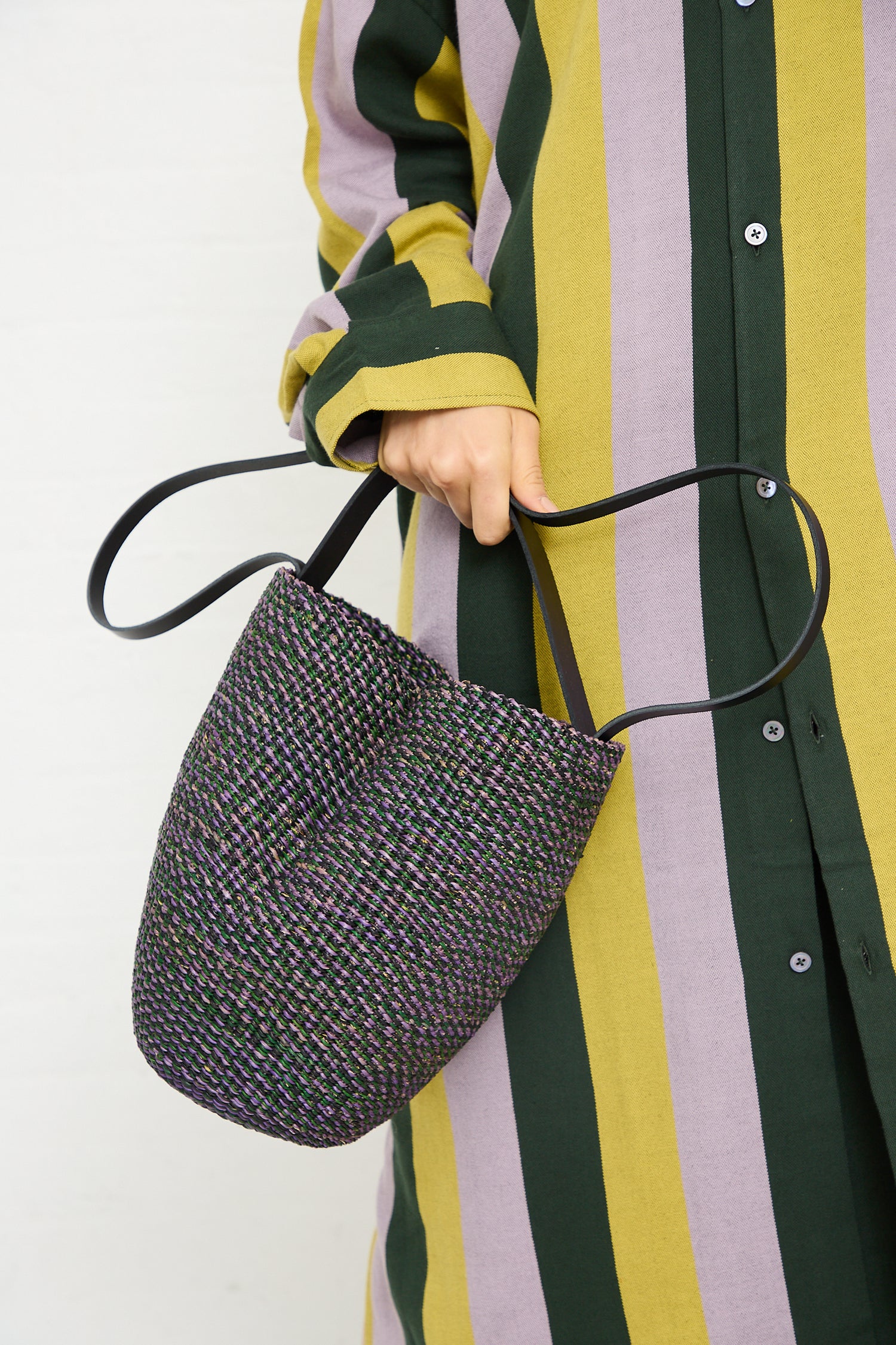 A person holding a N. 36 Haricot Bag in Green by Inès Bressand with vegetable-tanned leather handles while wearing a green and yellow striped shirt.