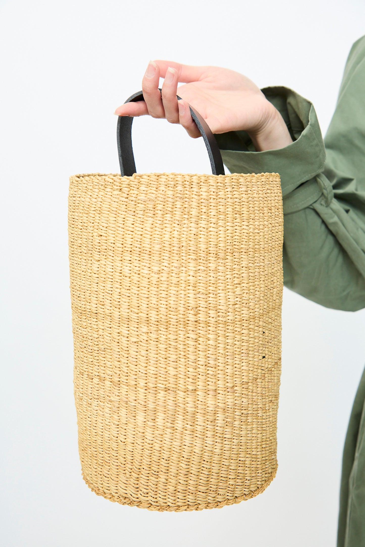 A person in a green sleeve holds the handwoven Seau Bag in Natural with Black by Inès Bressand from Ghana against a plain white background.
