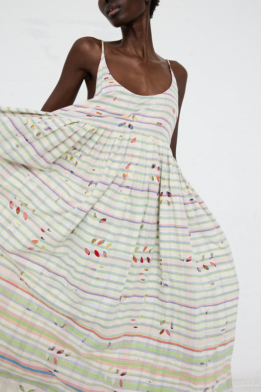 A woman in a flowing Injiri White Multi Stripe cotton slip dress, holding the fabric elegantly with one hand.
