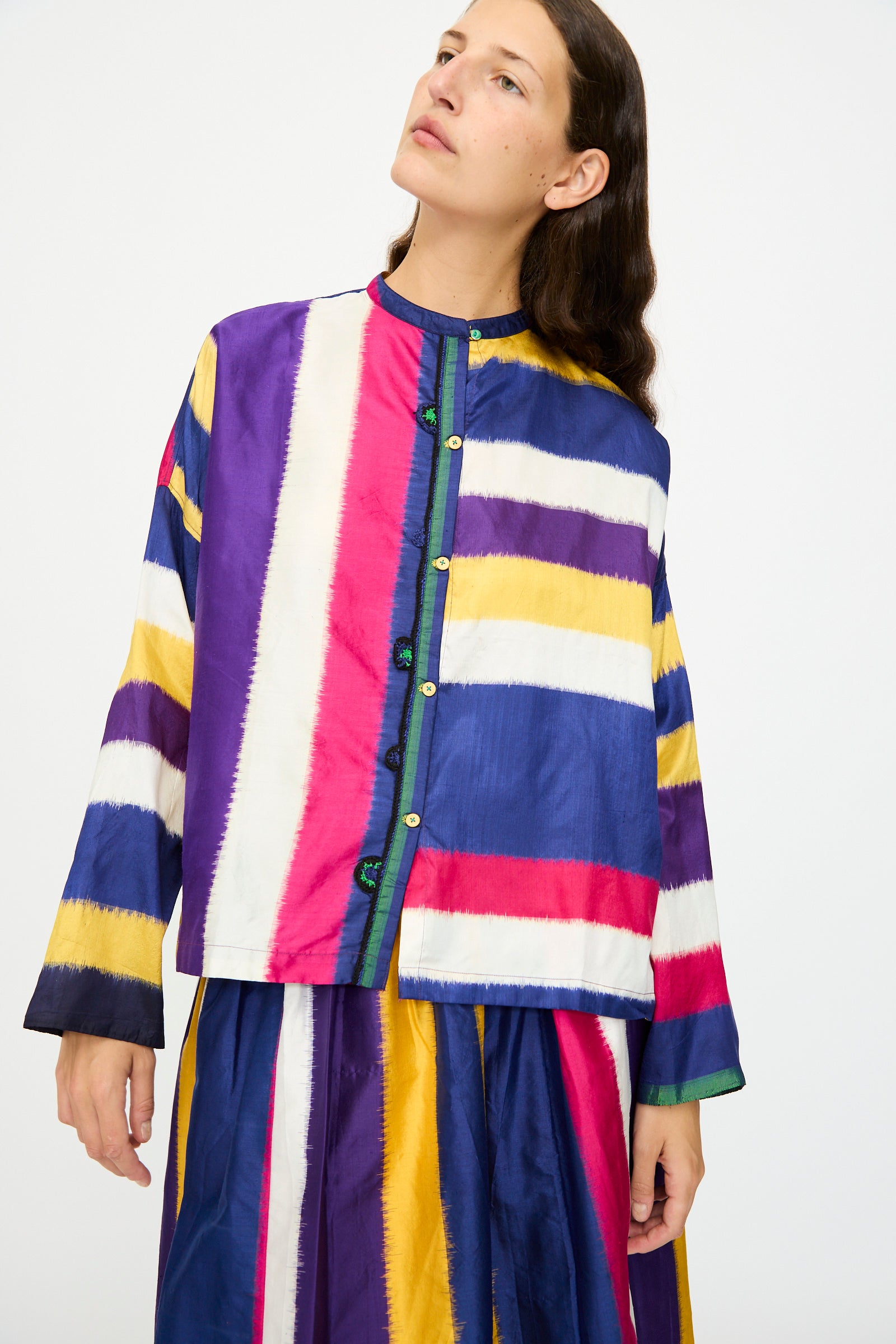 Wearing Injiri's Ikat Silk Shirt in Multi Stripe with a matching skirt, a person gazes upwards against a plain background.